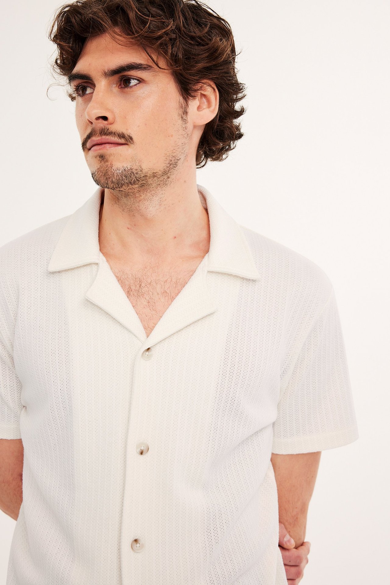 Edestä kuvattu mies yllään luonnonvalkoinen lyhythihainen resort-paita, jossa on kuvioitu neulos ja kolme nappia.