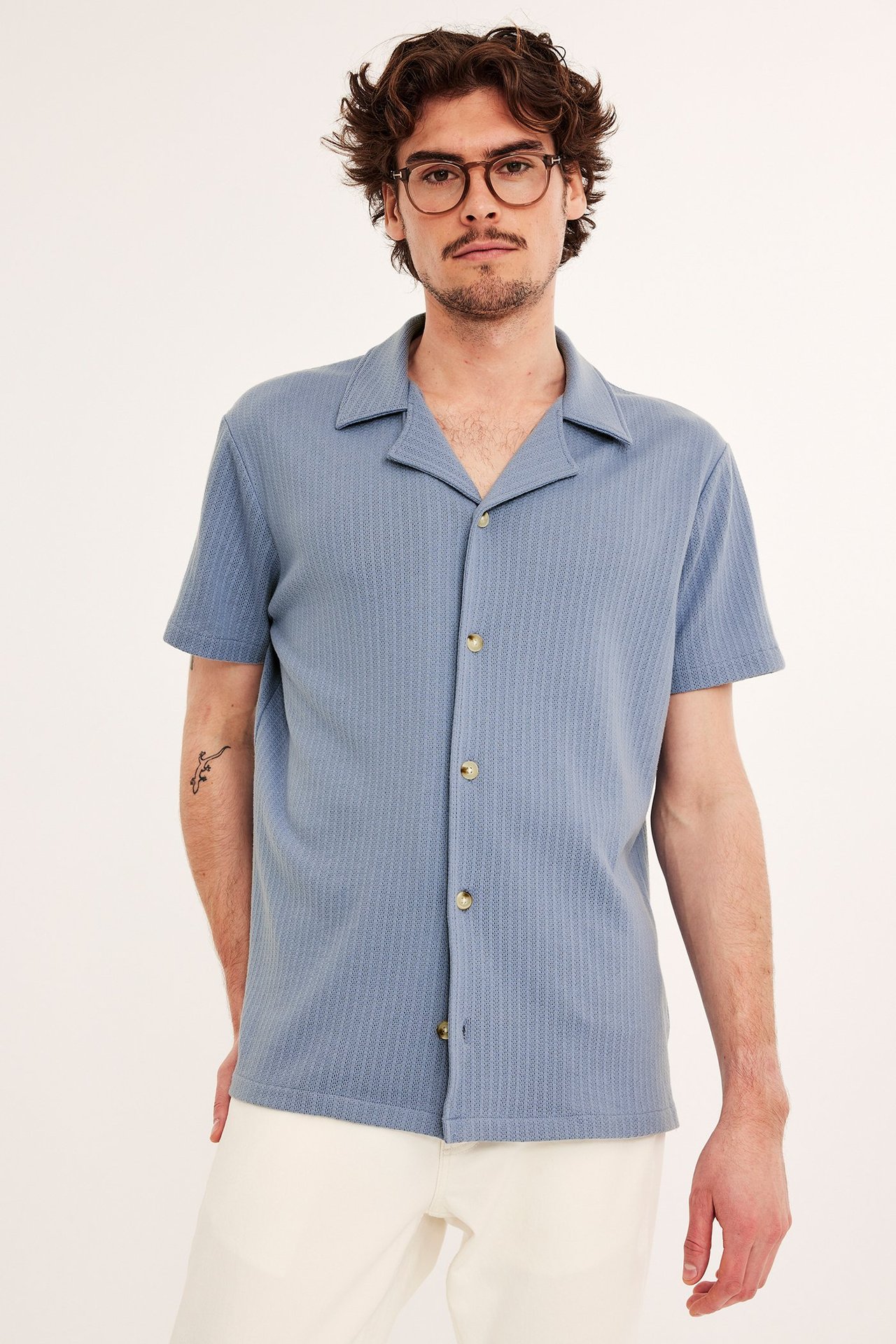 Edestä: mies laseissa, sininen kuvioitu resort-paita napeilla ja vaaleat housut.