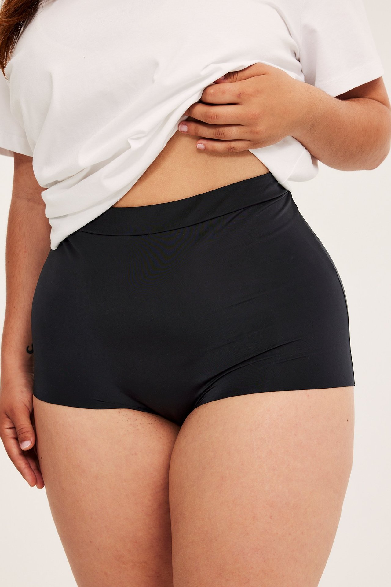 Framifrån, kvinna i svarta micro boxertrosor med resår i midjan och en vit t-shirt.