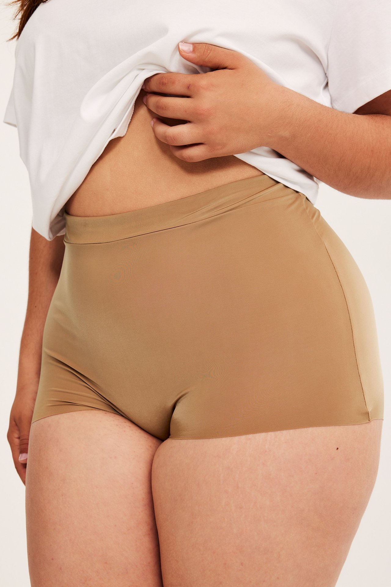 Närbild av en kvinna i bruna micro boxertrosor med resår i midjan, under en vit t-shirt.