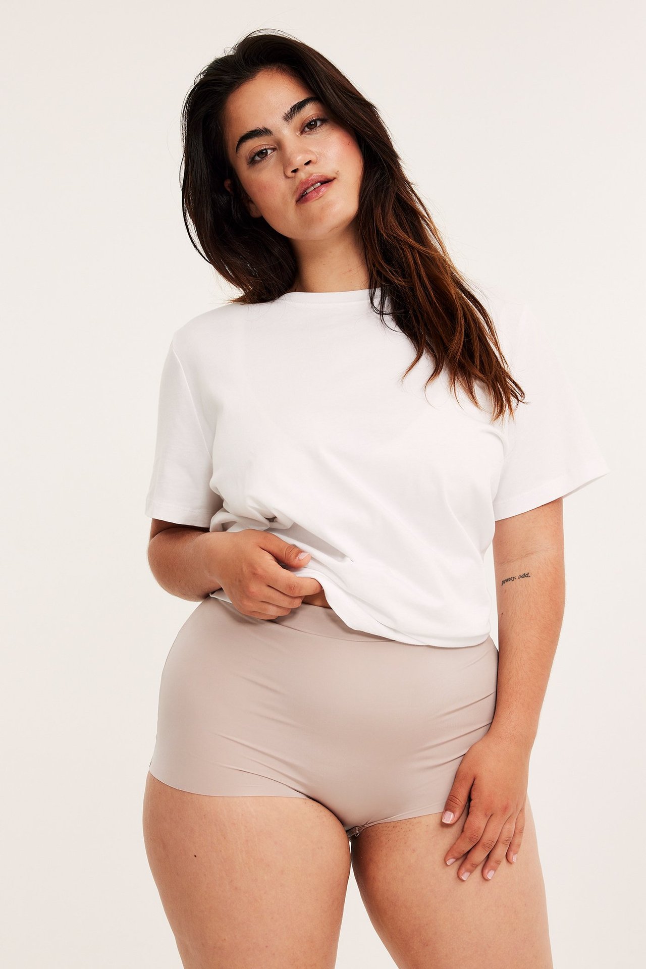 Forfra, kvinne i lys beige sømløs boxertruse og en hvit t-skjorte.