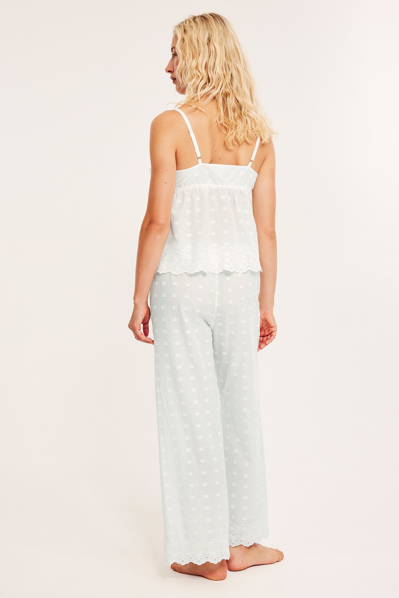 Naisen selkäkuva, yllään luonnonvalkoiset puuvillapyjamahousut kuvioinnilla ja broderie anglaise, sekä toppi.