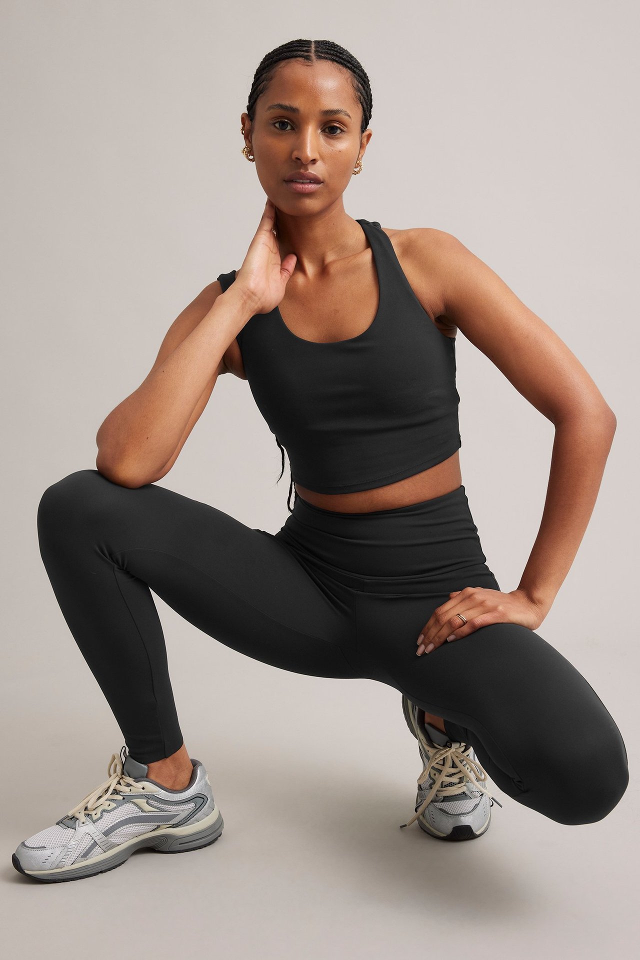 Framifrån: kvinna i svarta träningstights med ficka, svart sport-bh och ljusa sneakers.