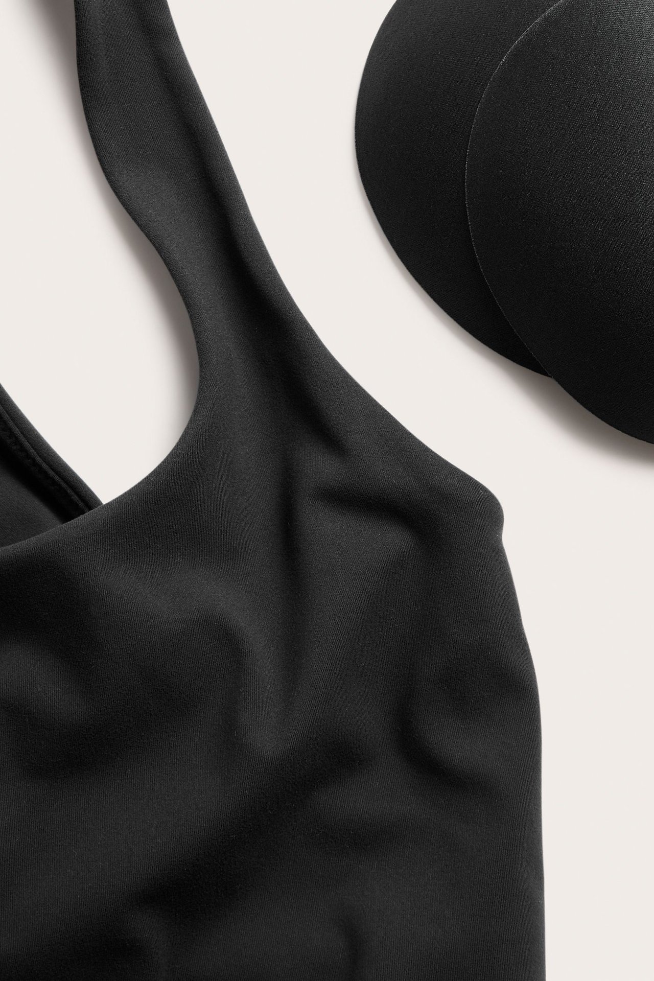 Zbliżenie czarnego topu sportowego z okrągłym dekoltem i dwoma czarnymi wyjmowanymi wkładkami.