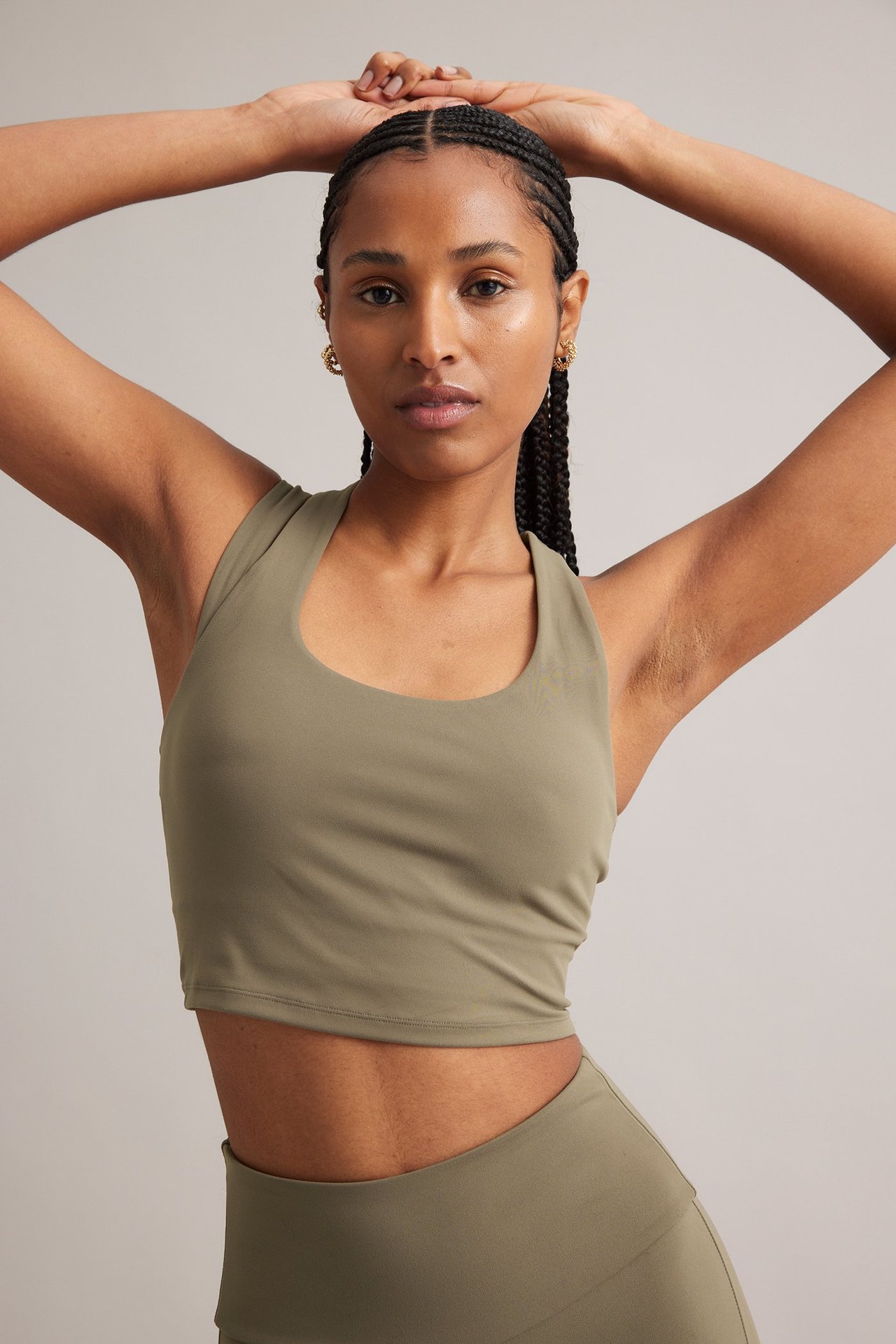 Edestä, nainen yllään oliivinvihreä pehmeä crop-urheilutoppi, yhteensopivat leggingsit ja pienet kultakorvakorut.