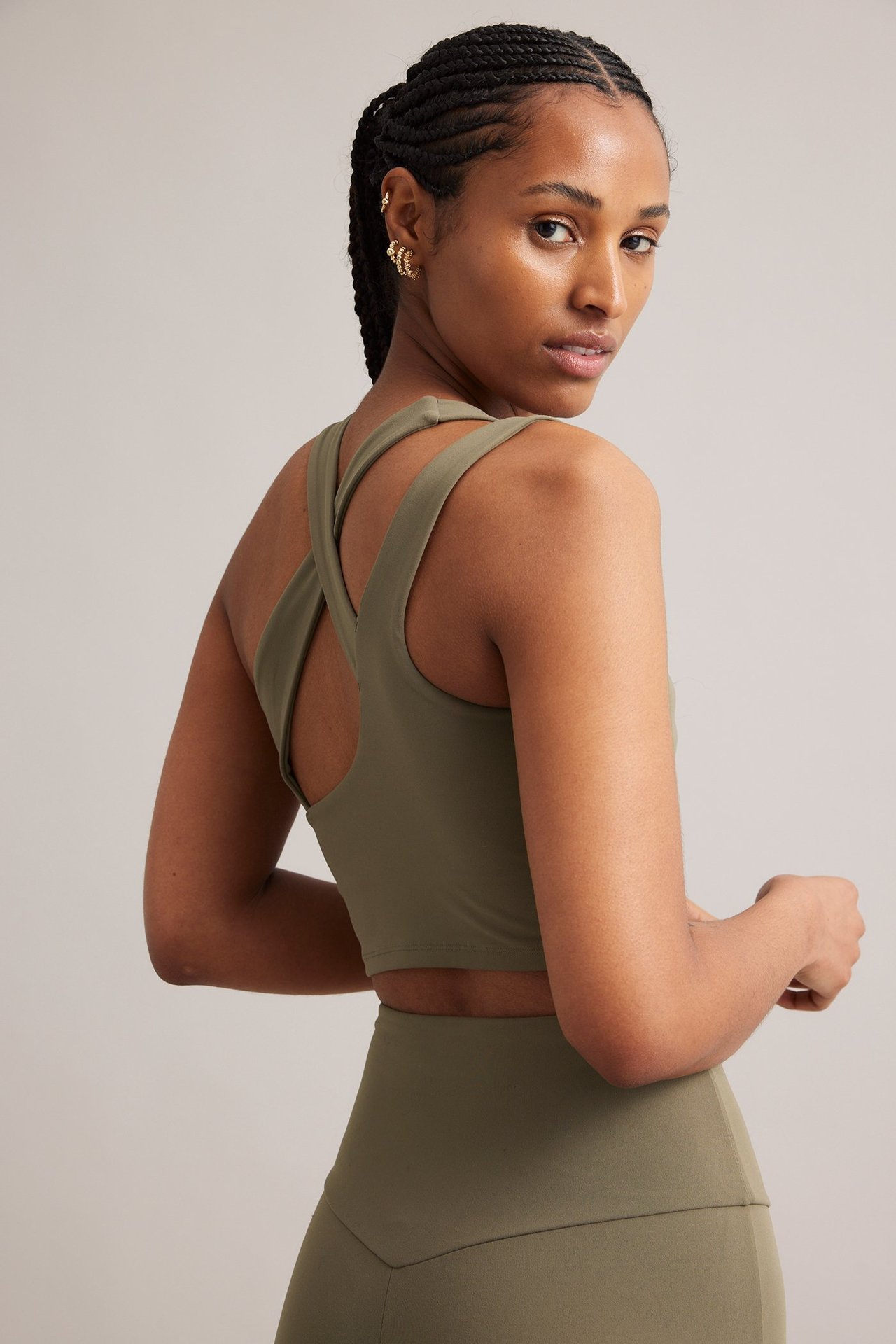 Nainen ruskeassa urheilutopissa, ristikko-olkaimet takana, yhteensopivat leggingsit ja kultaiset korvakorut.