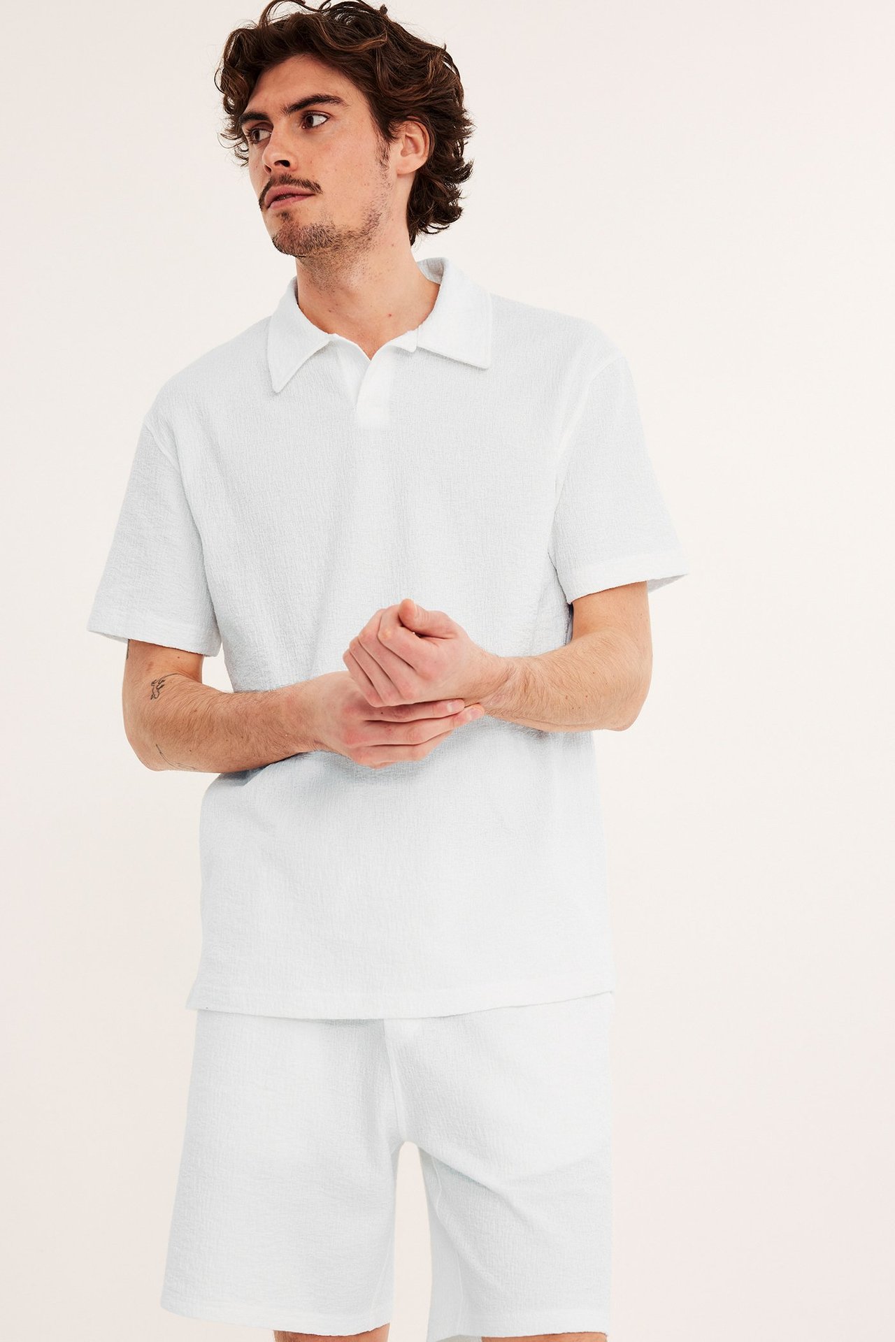 Edestä kuvattu mies yllään luonnonvalkoinen lyhythihainen strukturoitu pikeepaita ja yhteensopivat shortsit.