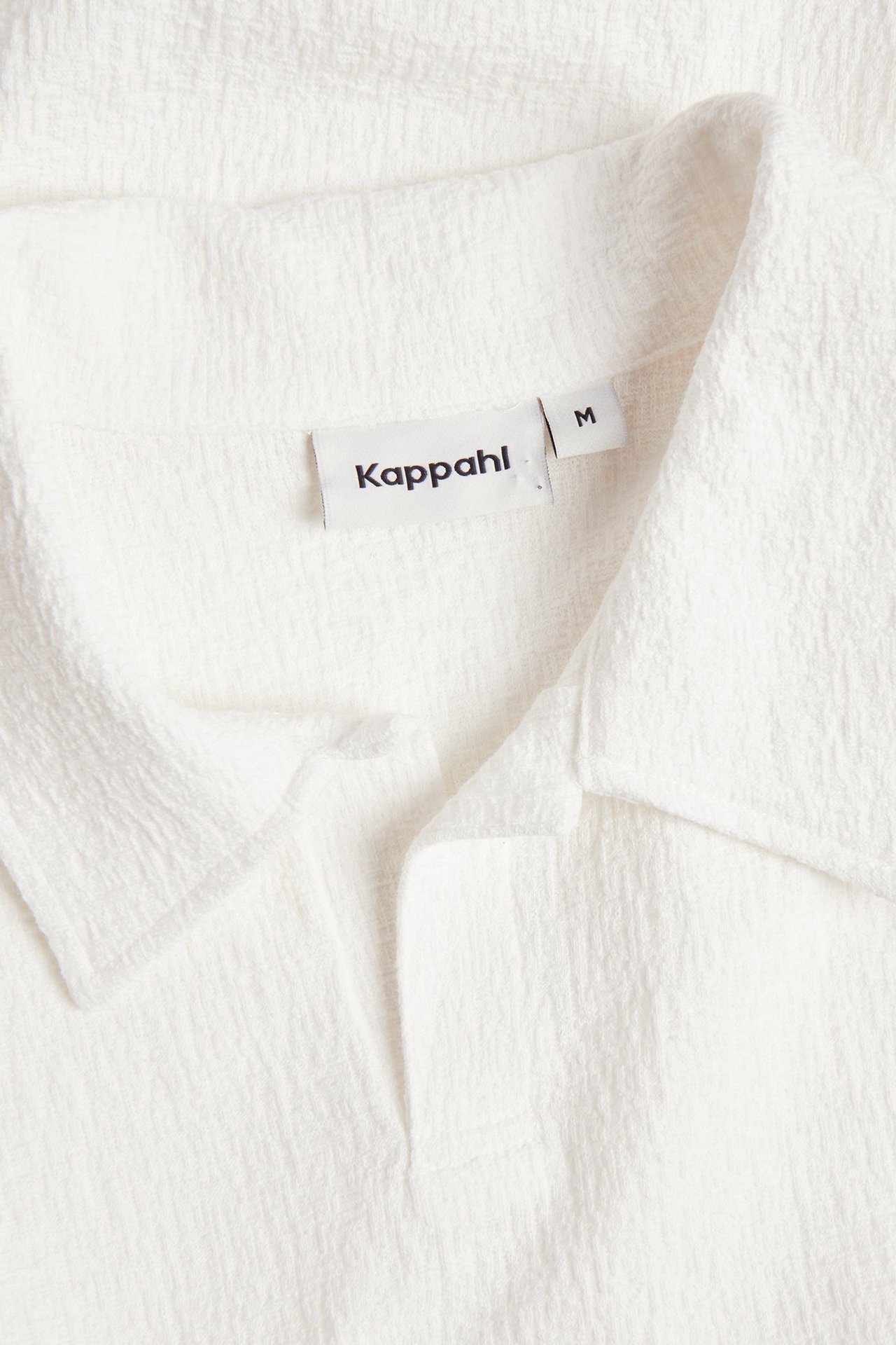 Zbliżenie na męską koszulkę polo w kolorze ecru ze strukturalnym wzorem, kołnierzykiem i dekoltem V.