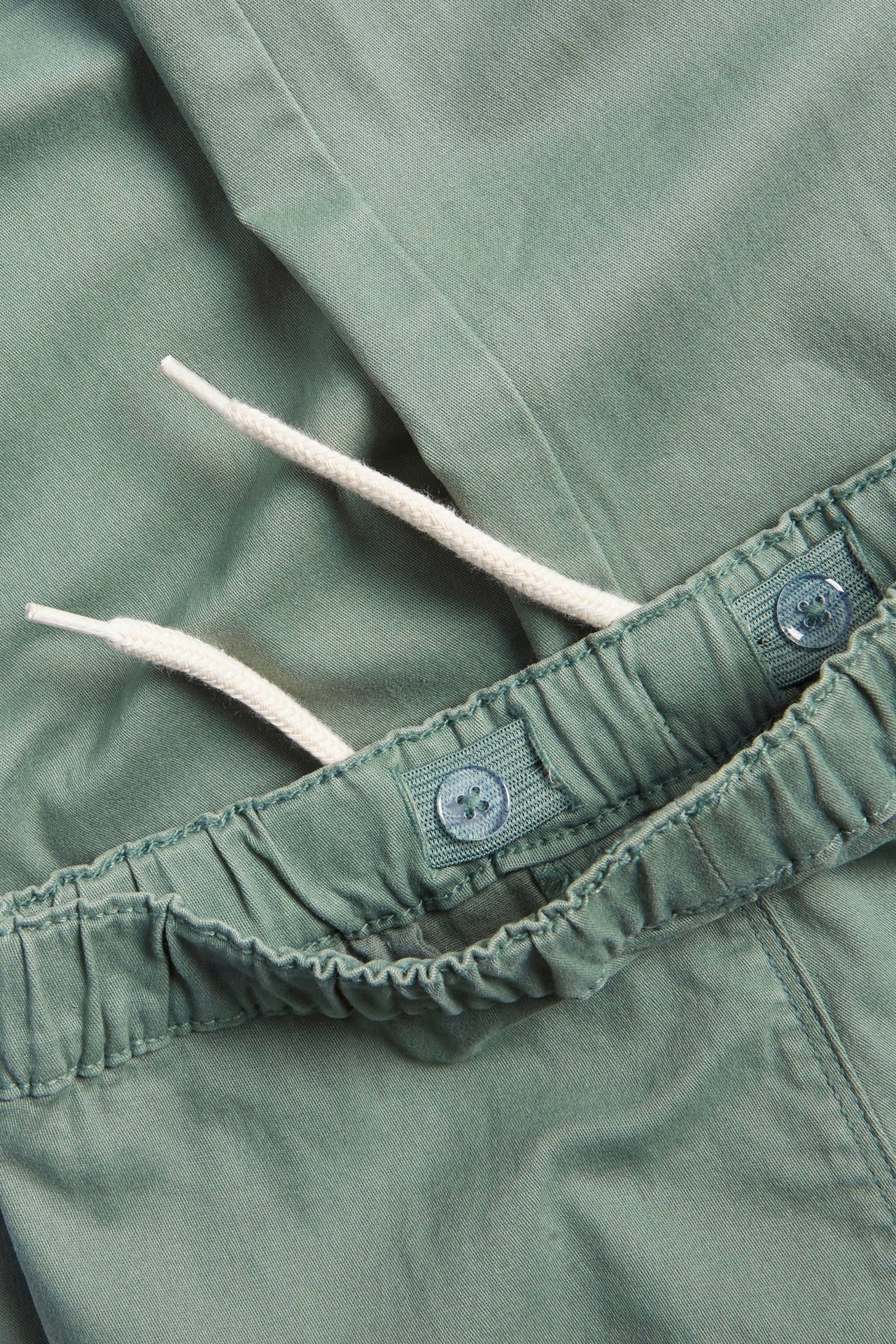 Zbliżenie zielonych bawełnianych spodni cargo z elastyczną talią, białym sznurkiem i regulowanymi guzikami.