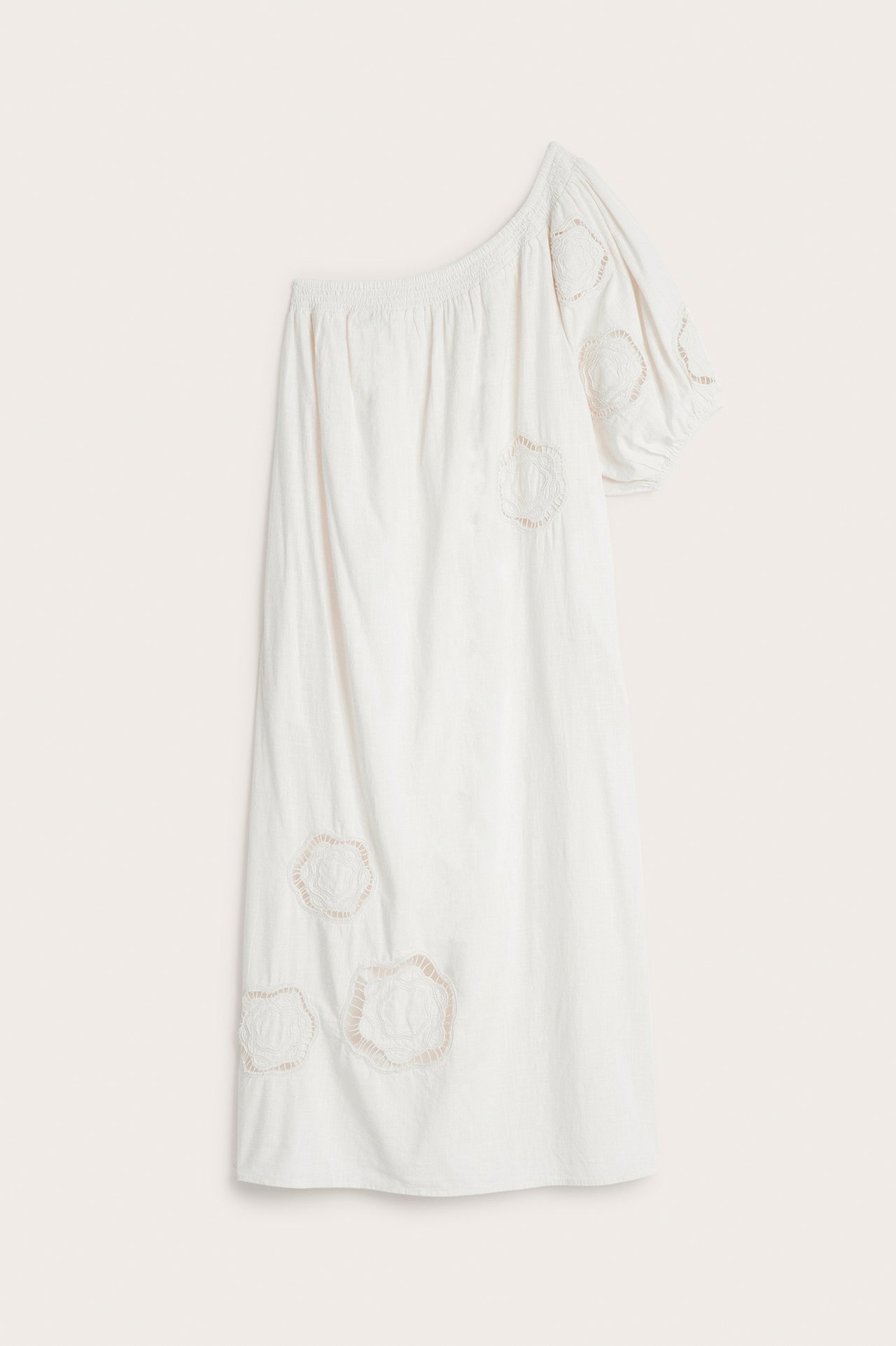 Frontvisning av en hvit bomulls one-shoulder kjole med blomsterapplikasjoner og elastisk halslinning.