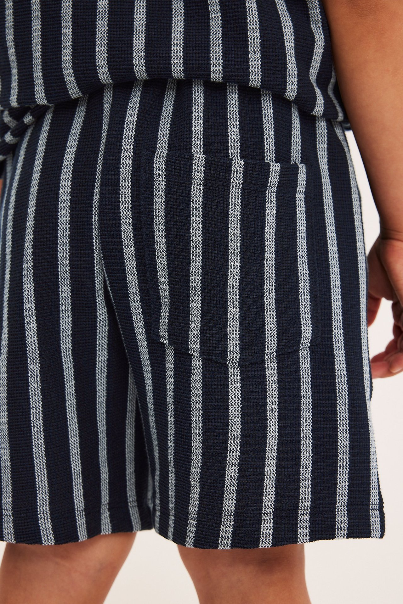 Närbild, bakifrån: Randiga shorts i mörkblå och vit bomull med ficka, bärs av ett barn.