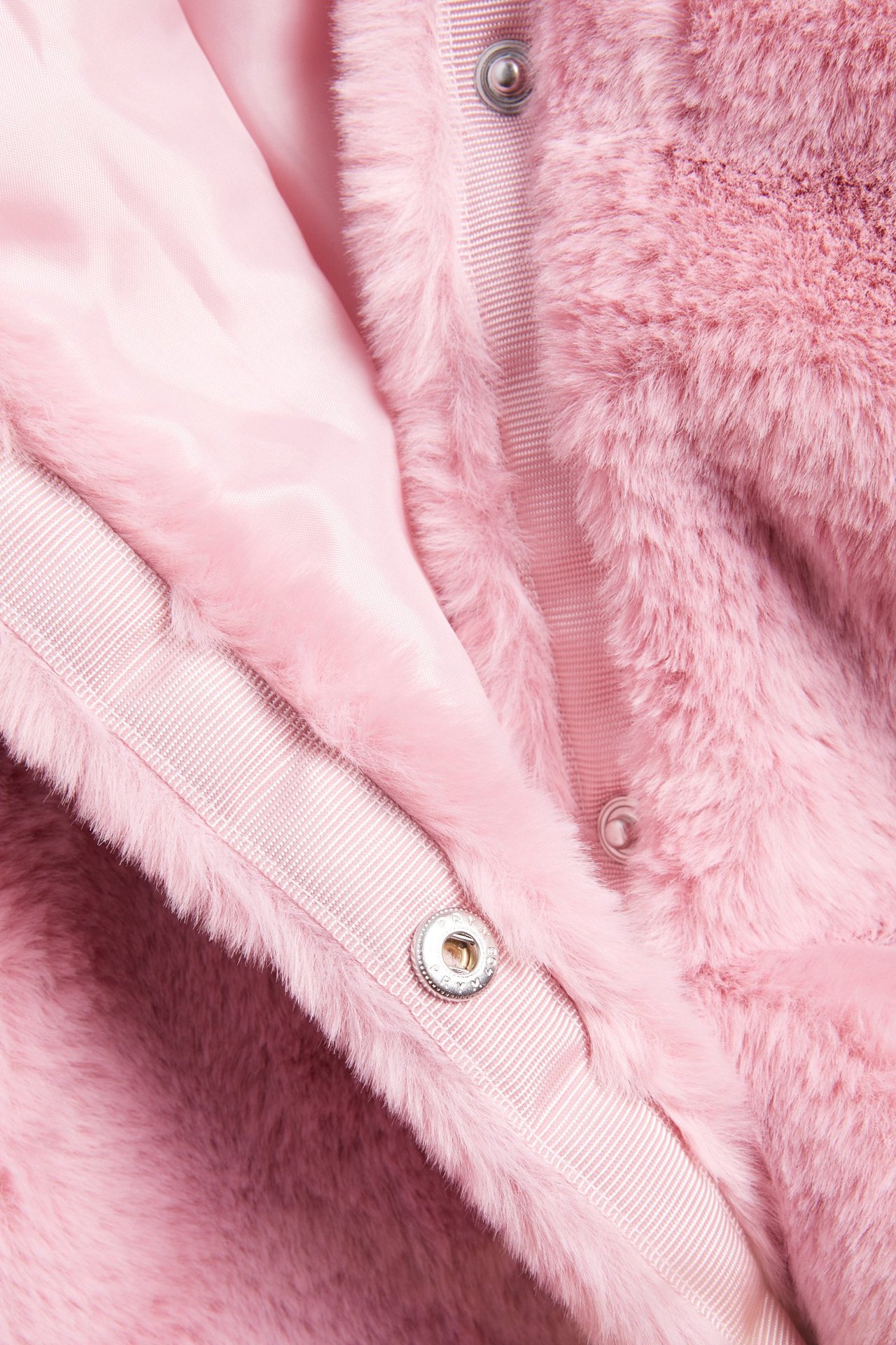 Zbliżenie jasnoróżowej kurtki ze sztucznego futra z zatrzaskami i satynową podszewką.