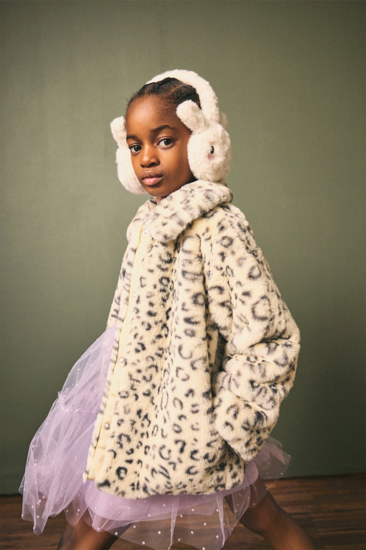 Framifrån: Barn i beige leopardmönstrad fuskpälsjacka, ljuslila tyllkjol och vita kaninöronmuffar.