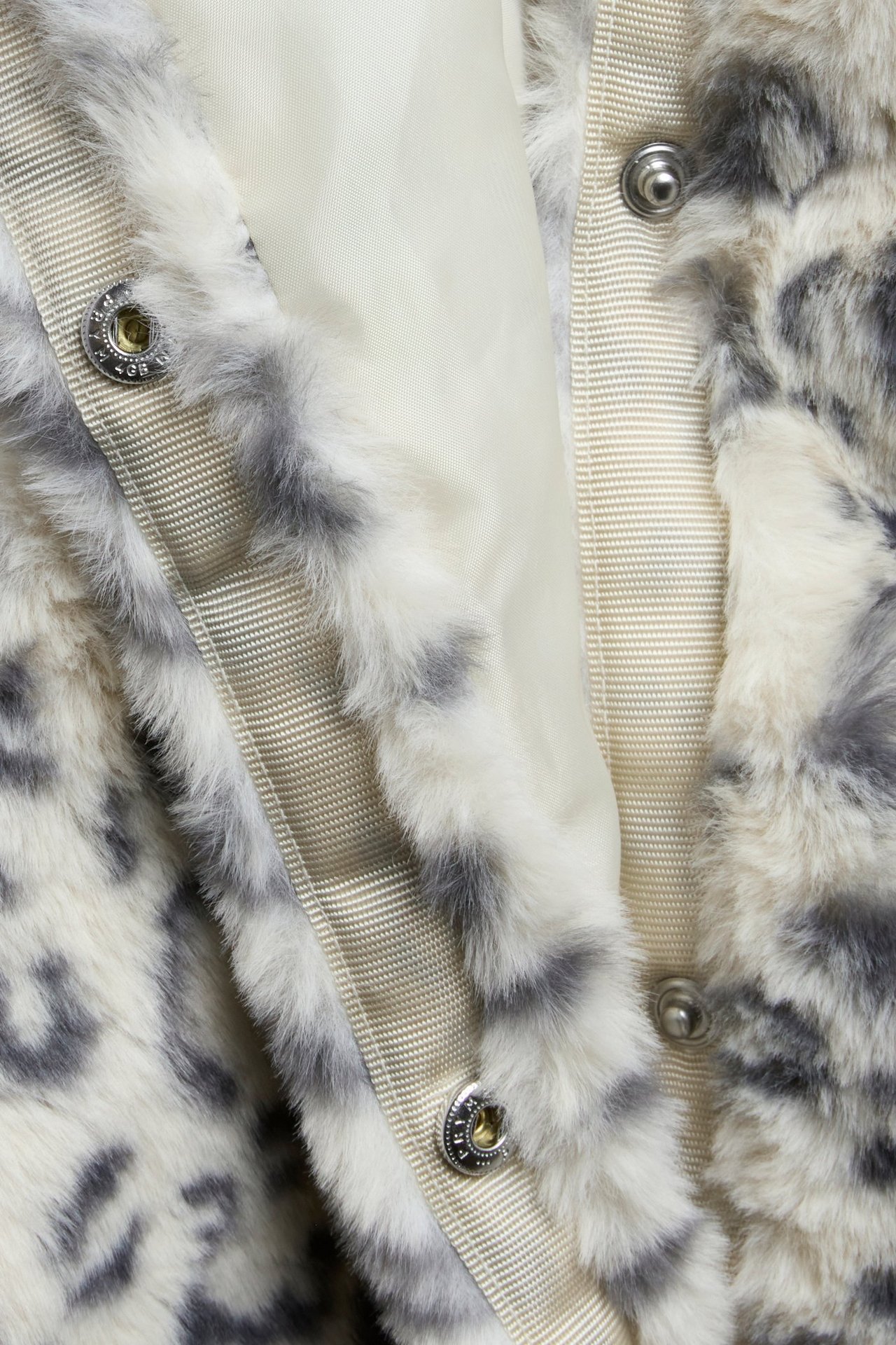 Zbliżenie beżowej kurtki ze sztucznego futra w panterkę z zatrzaskami.
