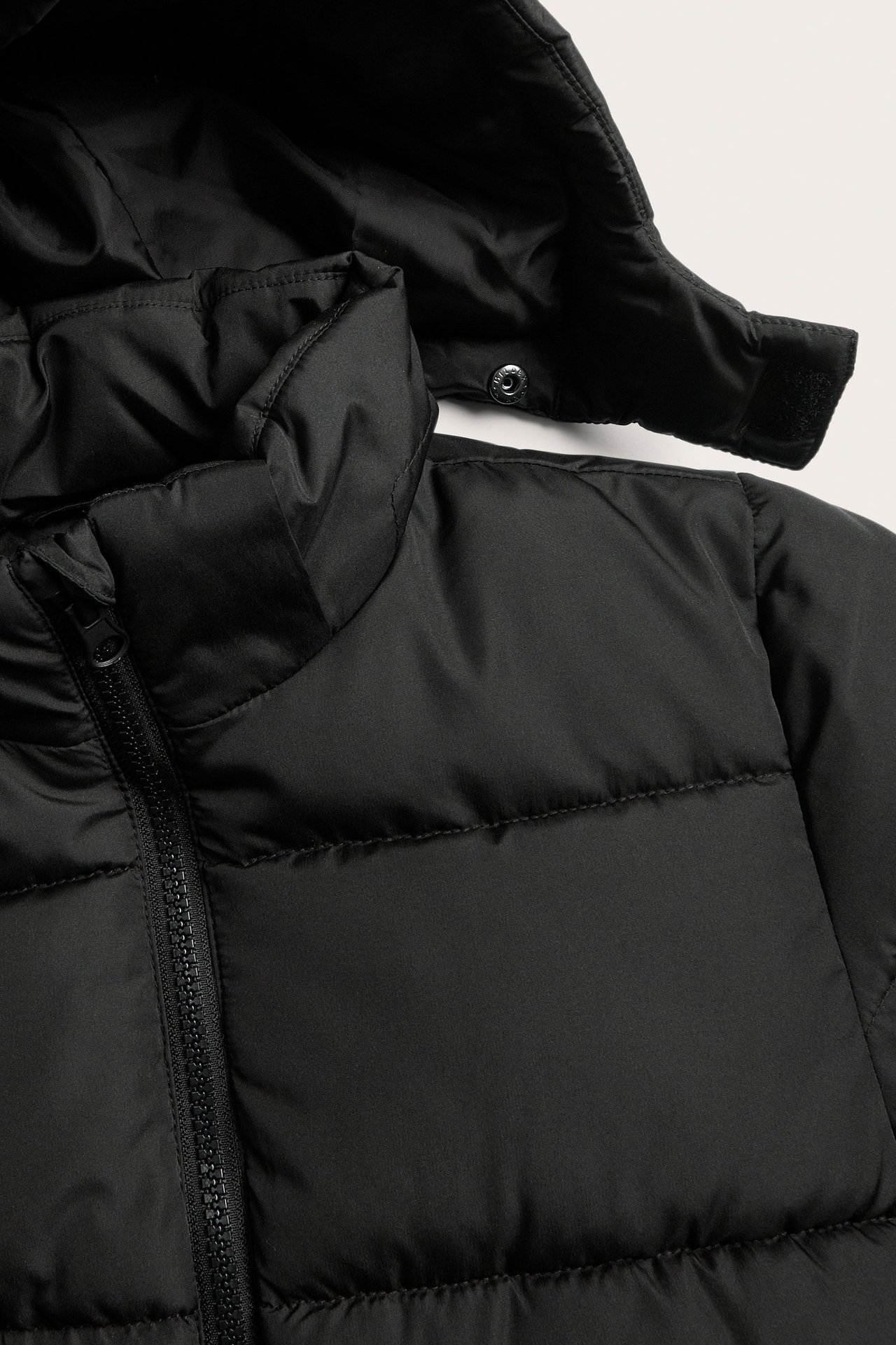 Zbliżenie czarnej pikowanej kurtki puchowej z zamkiem błyskawicznym, wysokim kołnierzem i odpinanym kapturem.