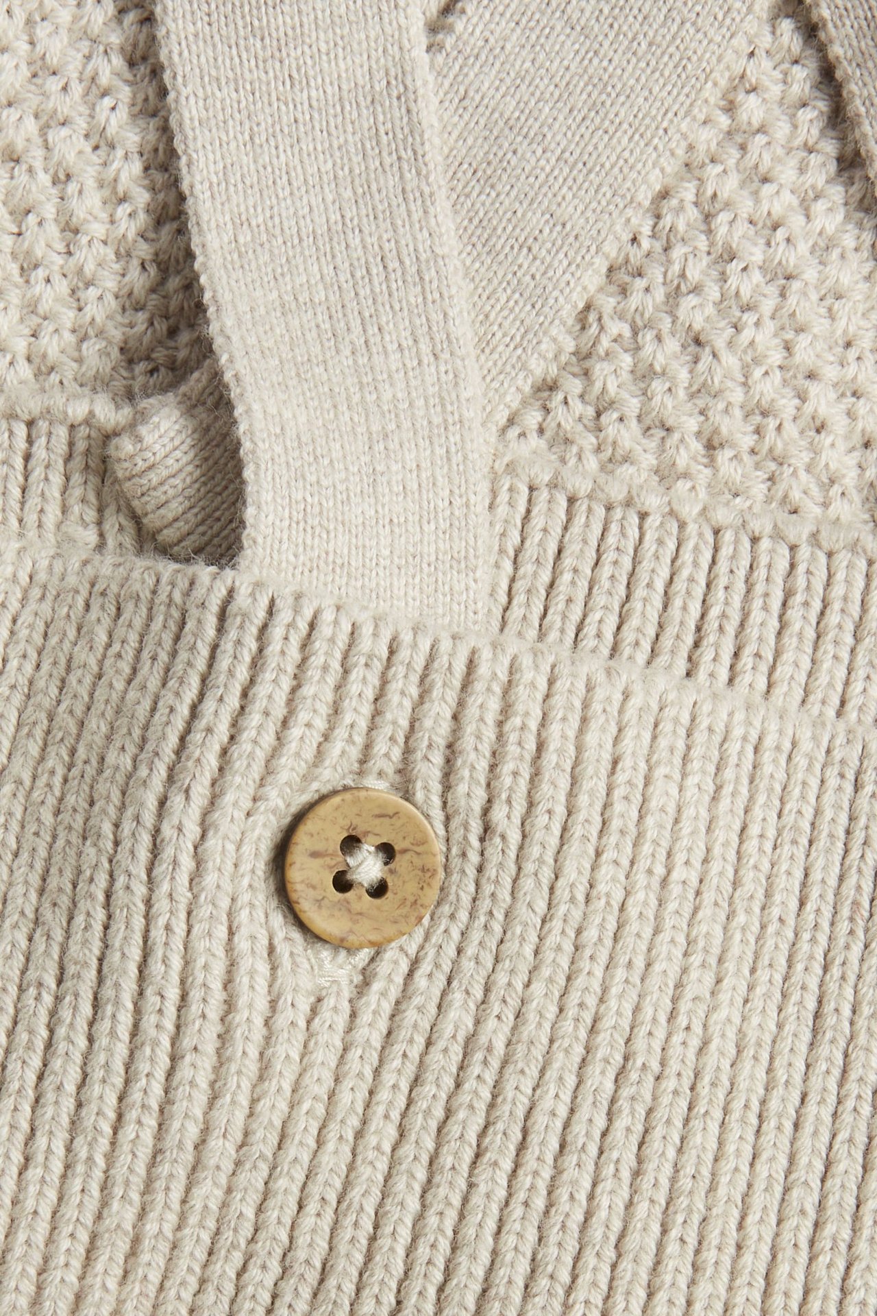 Nærbilde av beige melert strukturstrikket babyselebukse med stropp og treknapp.