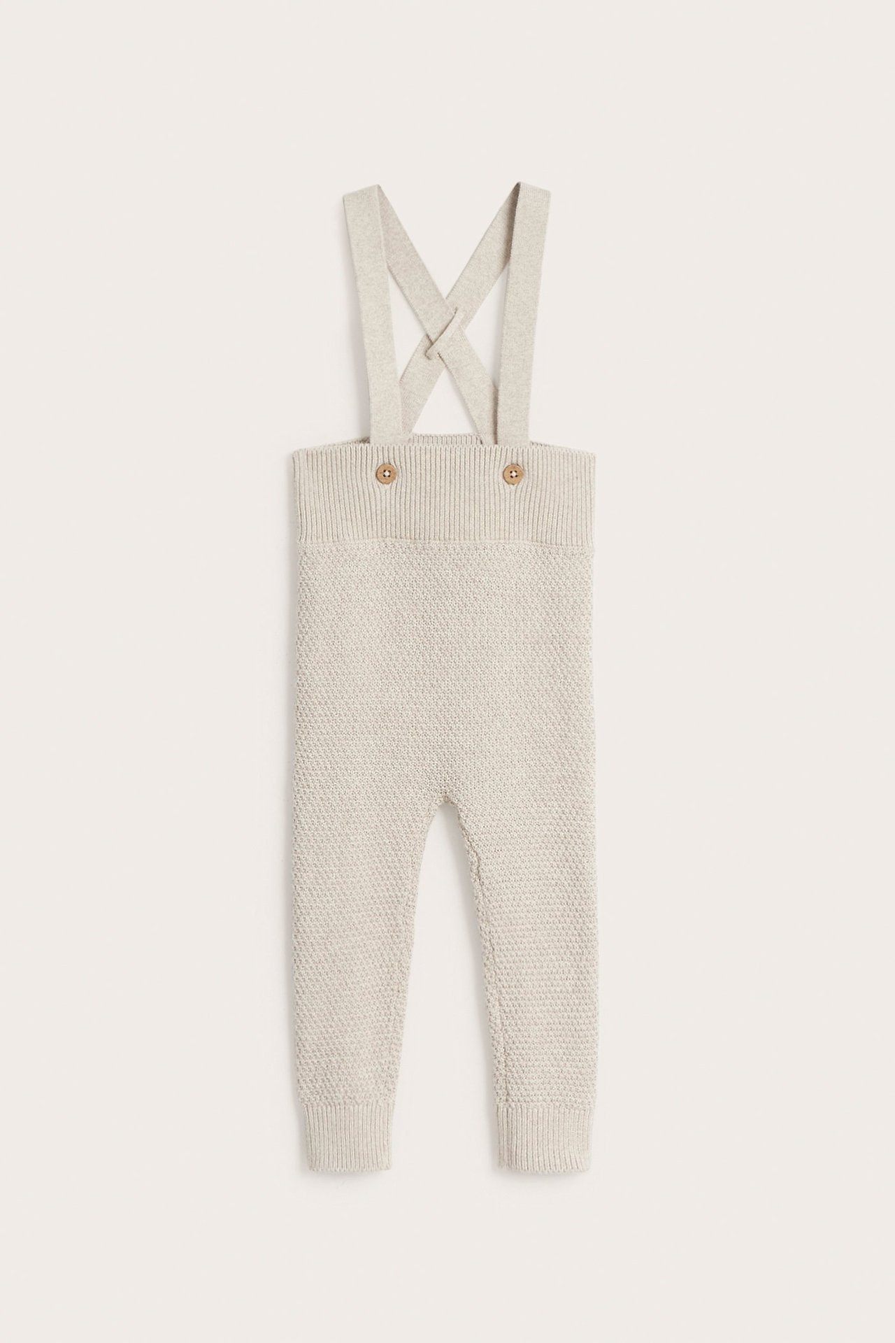 Frontalvisning av beige melert, strukturstrikket bomullsselebukse for baby, med justerbare seler og knapper.