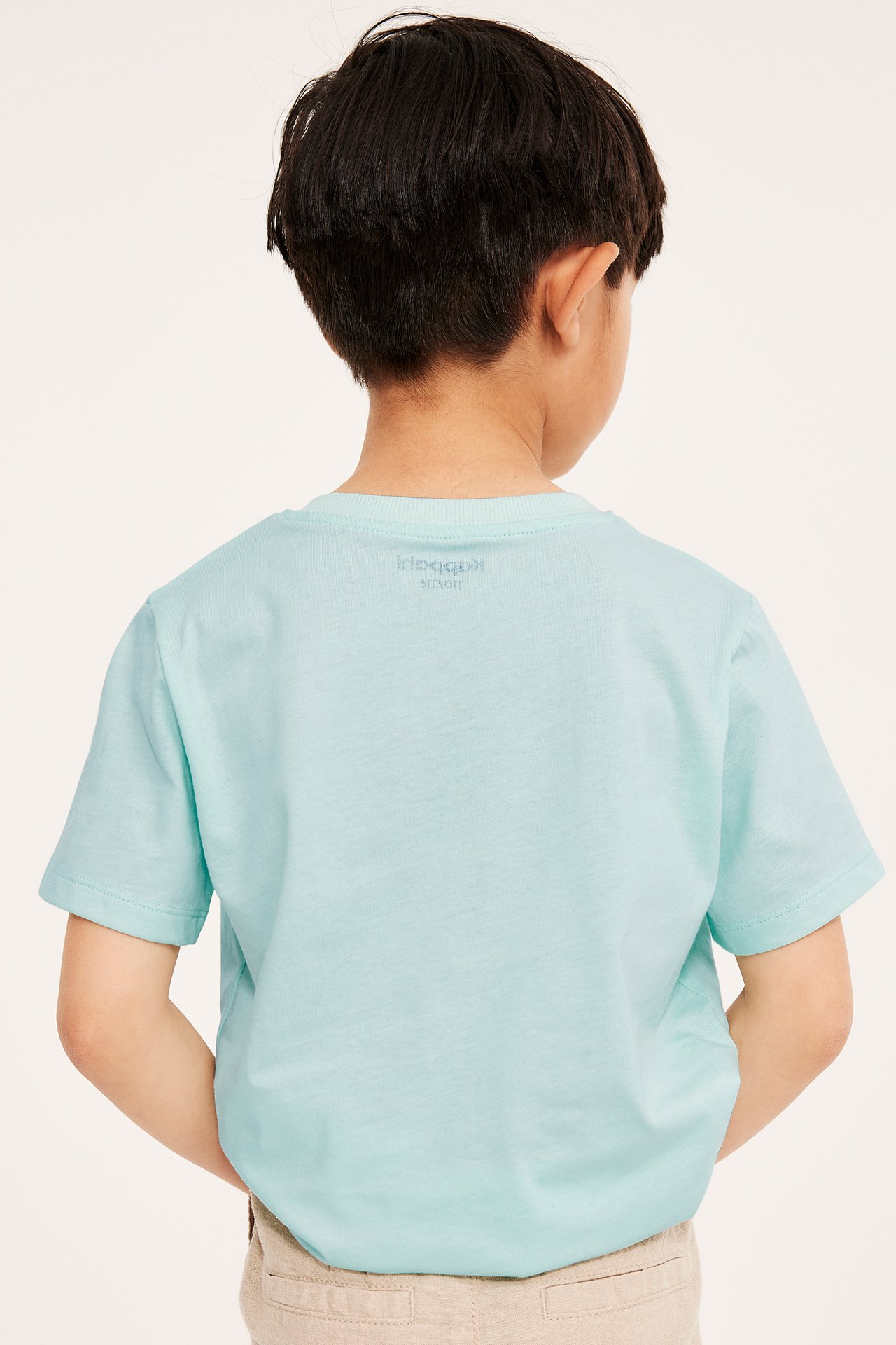 Widok z tyłu dziecka w jasnoturkusowym bawełnianym T-shircie i beżowych szortach.