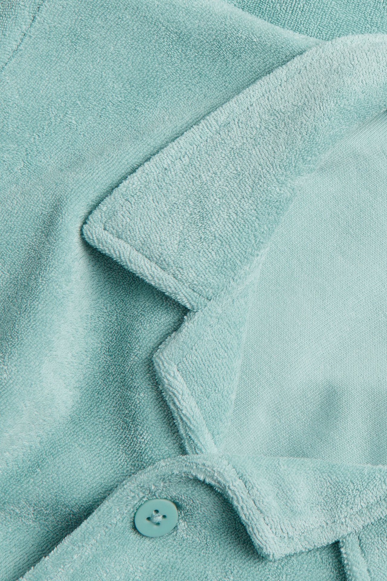 Närbild av en ljusgrön kortärmad frottéskjorta med resortkrage och en knapp.