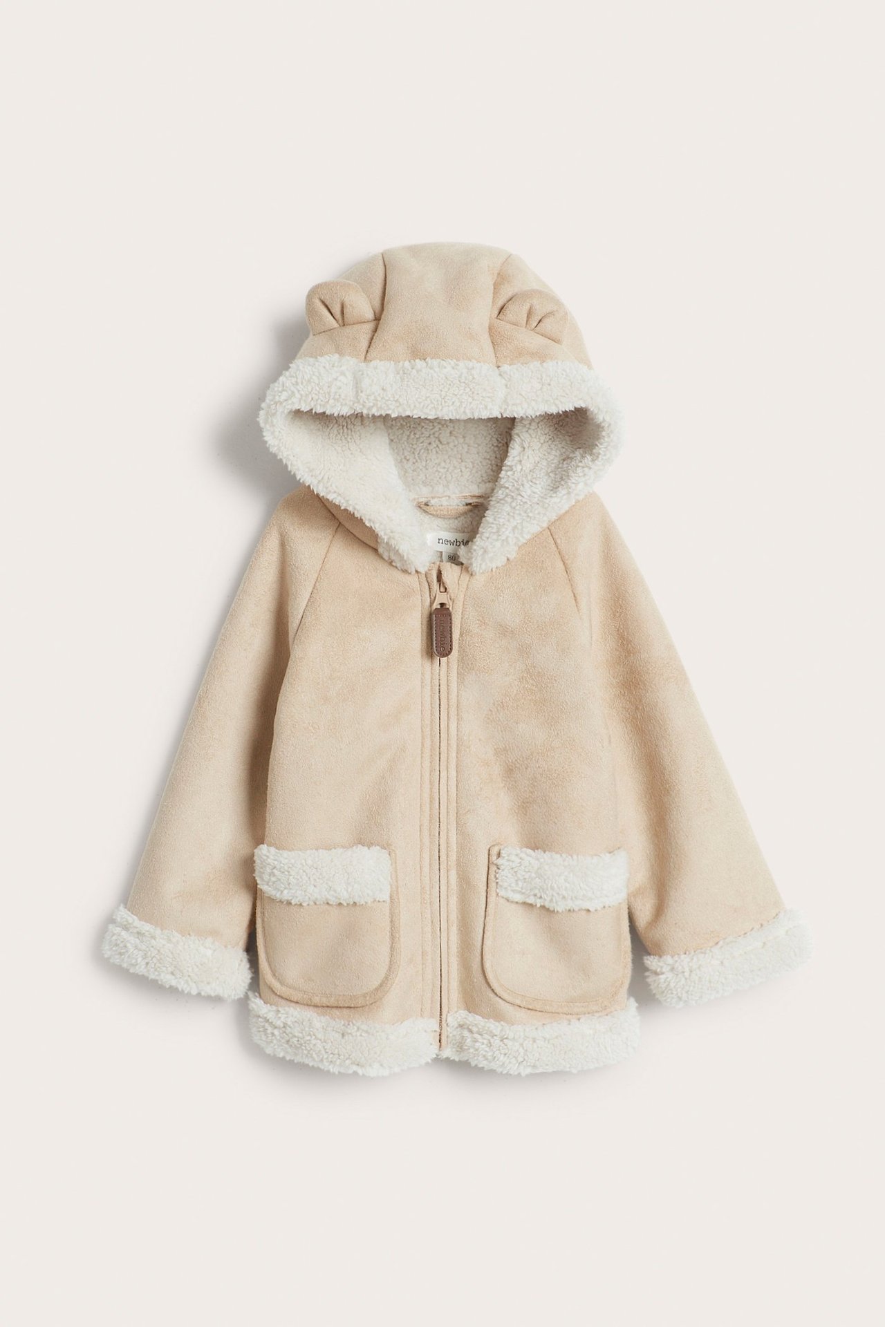 Edestä: Lasten beige tekomokka-shearlingtakki, jossa pörrövuori, korvahuppu, vetoketju ja taskut.