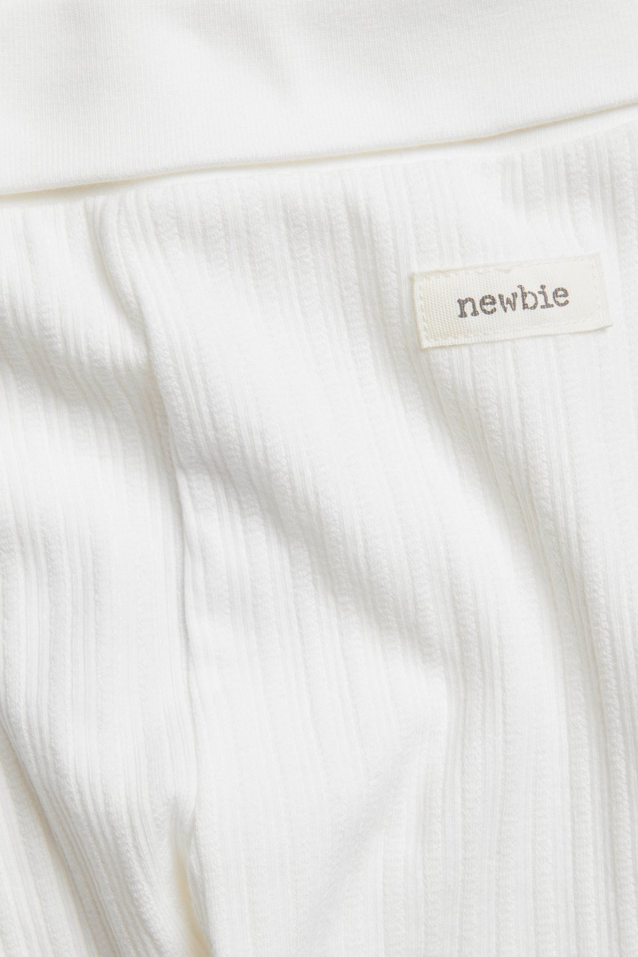 Zbliżenie na ecru prążkowany materiał legginsów z metką "newbie".