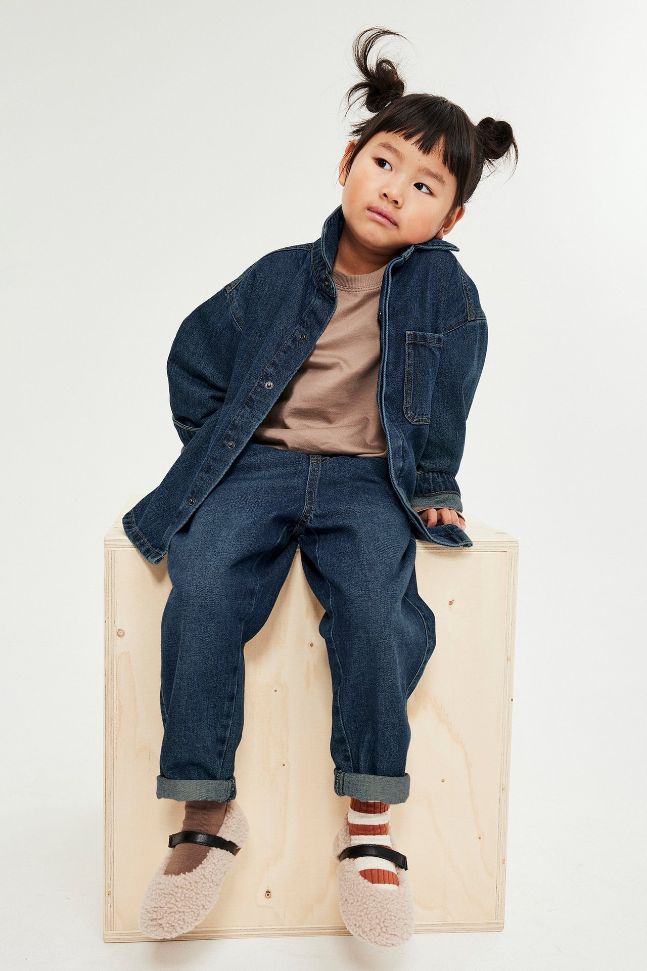 Forfra: Barn iført mørk denimjeans, en brun T-skjorte, åpen denimjakke og lodne sko.