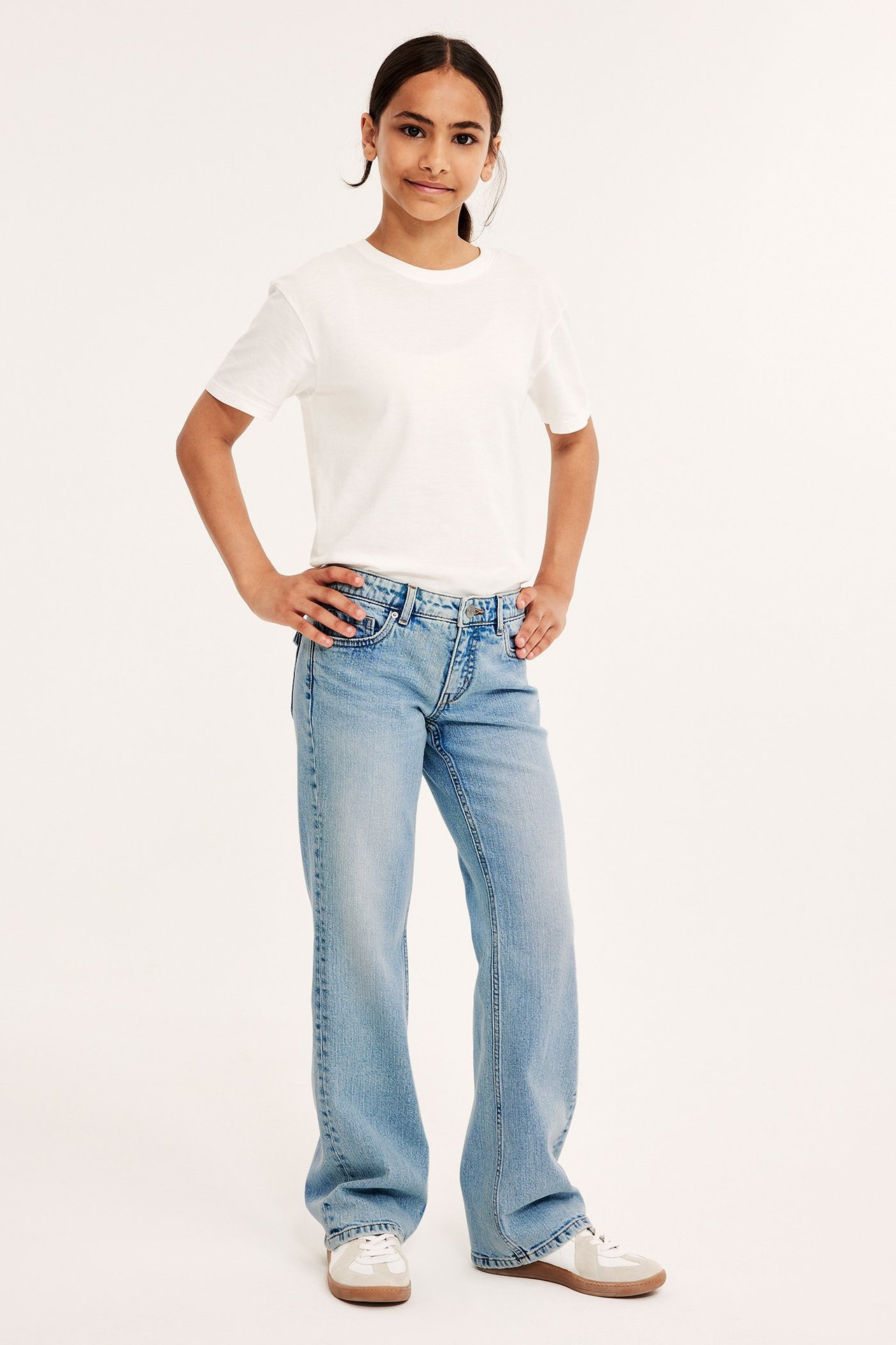 Lågmidjade bootcut jeans i ljusblått med bakfickor med ficklock, på ung kvinna i vit t-shirt.