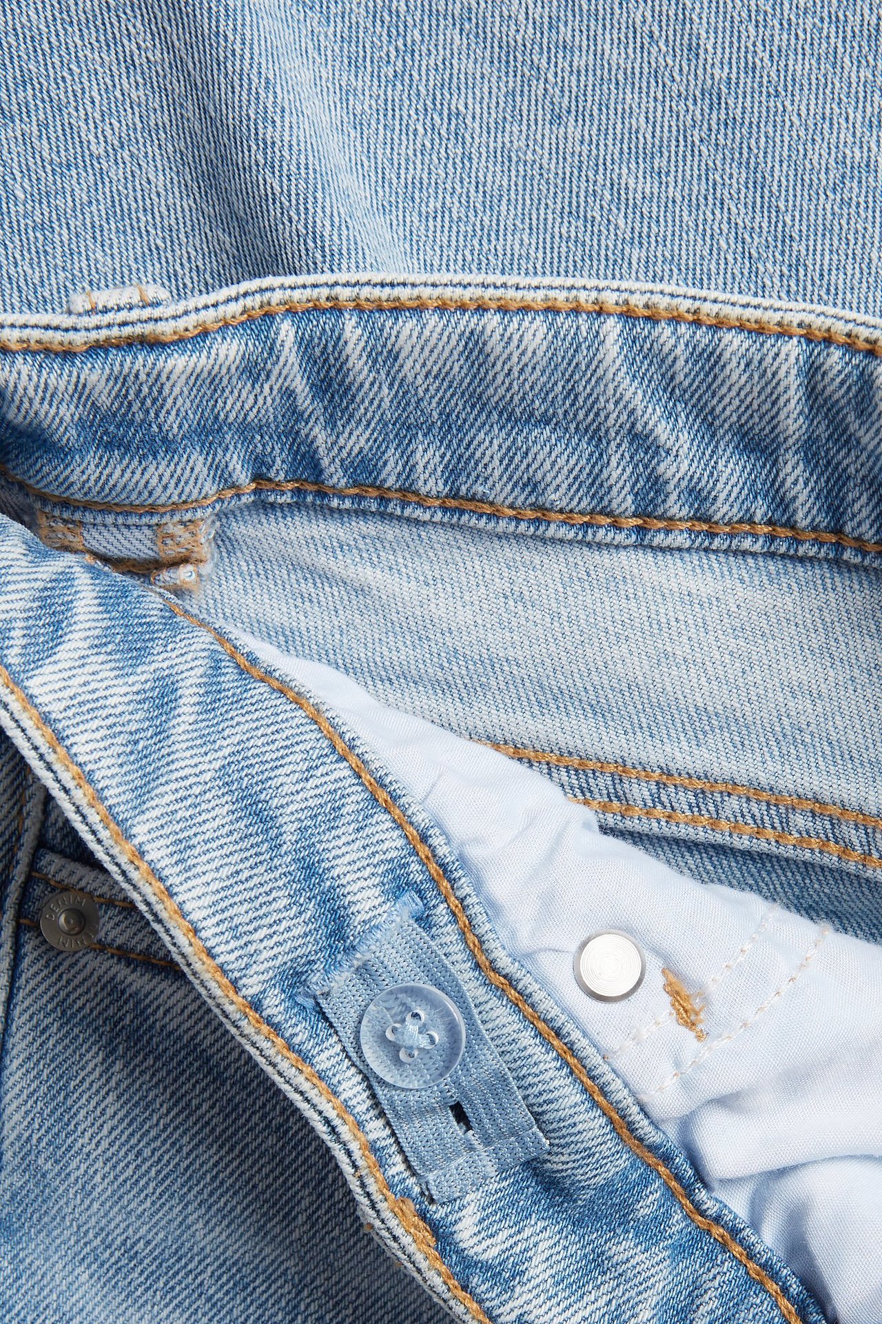 Zbliżenie na jasnoniebieskie jeansy bootcut z niskim stanem, regulowaną gumką i zapięciem na guzik.