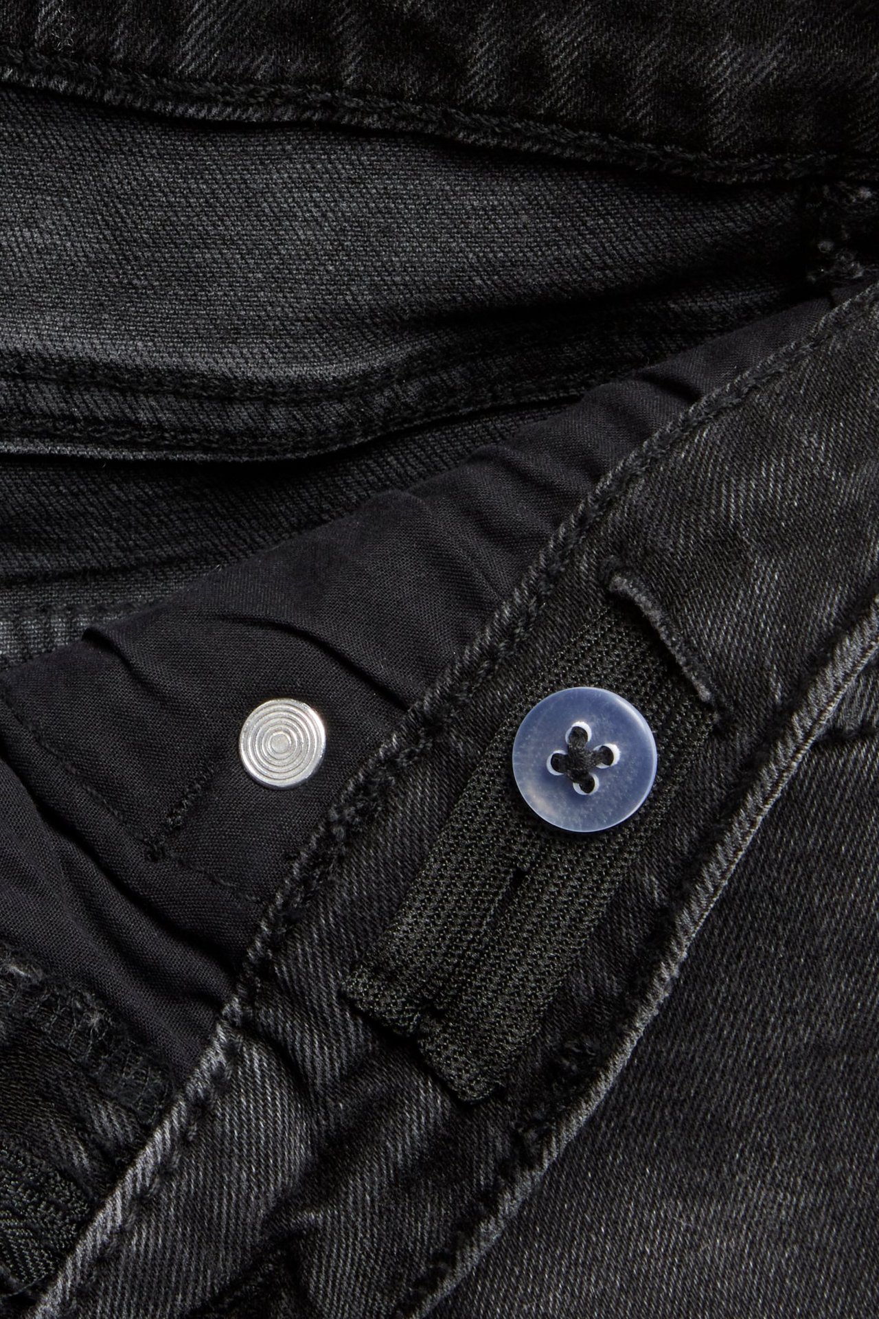 Zbliżenie na szare dżinsy bootcut z regulowaną gumką w pasie, srebrnym guzikiem i niebieskim guzikiem.