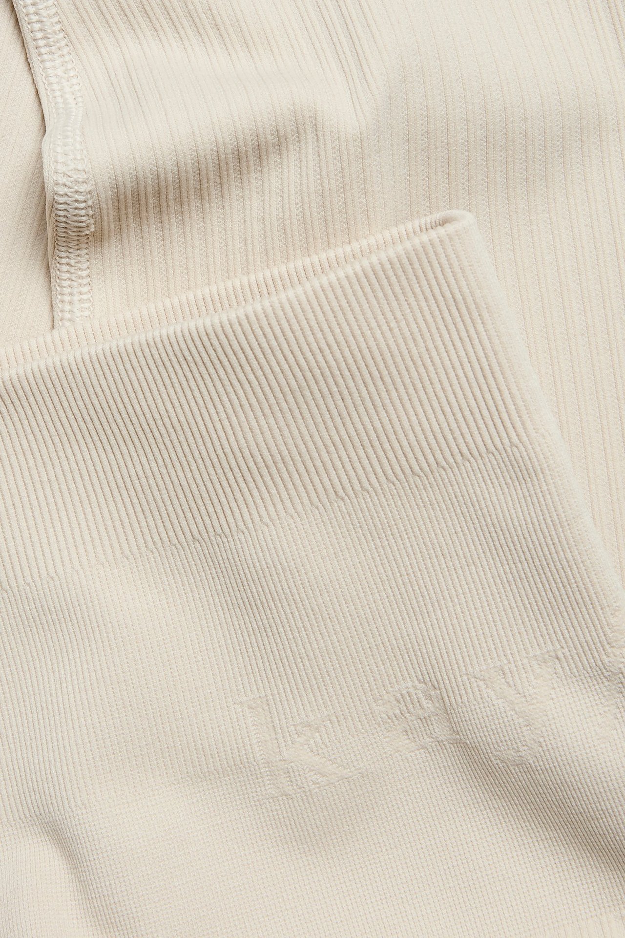 Zbliżenie jasnobeżowych prążkowanych bezszwowych legginsów treningowych z subtelnym detalem logo.