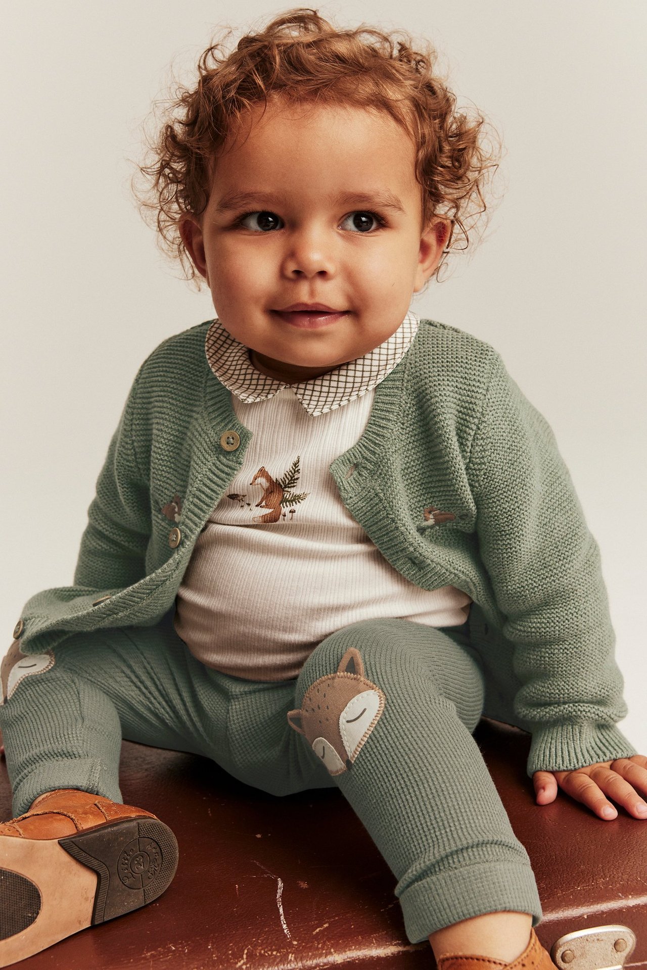 Edestä: Vauva vihreässä neuleneuletakissa, valkoisessa kettupainatuspaidassa ja vihreissä kettuleggingseissä.