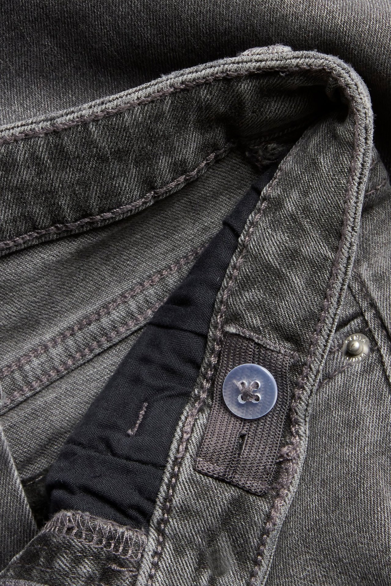 Zbliżenie na pas szarych jeansów bootcut, pokazujące regulowaną wewnętrzną gumkę z guzikiem.