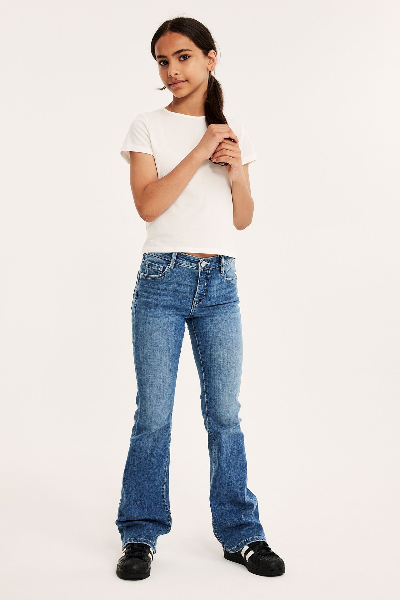 Tonårsflicka i vit T-shirt och blå bootcut jeans med låg midja, bakfickor, justerbar midja.