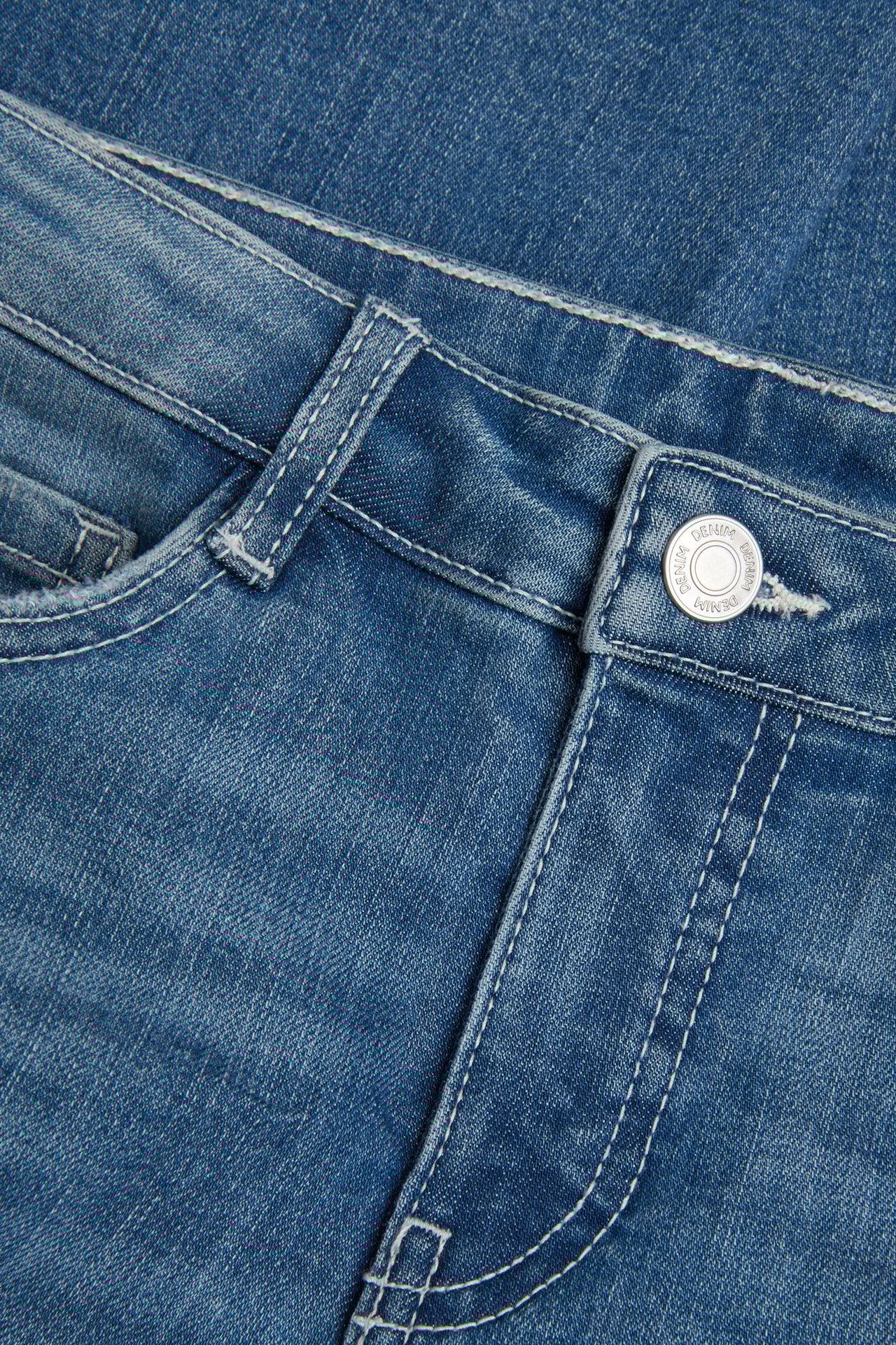 Zbliżenie na niebieskie dżinsy bootcut z niskim stanem, srebrnym guzikiem i białymi szwami.