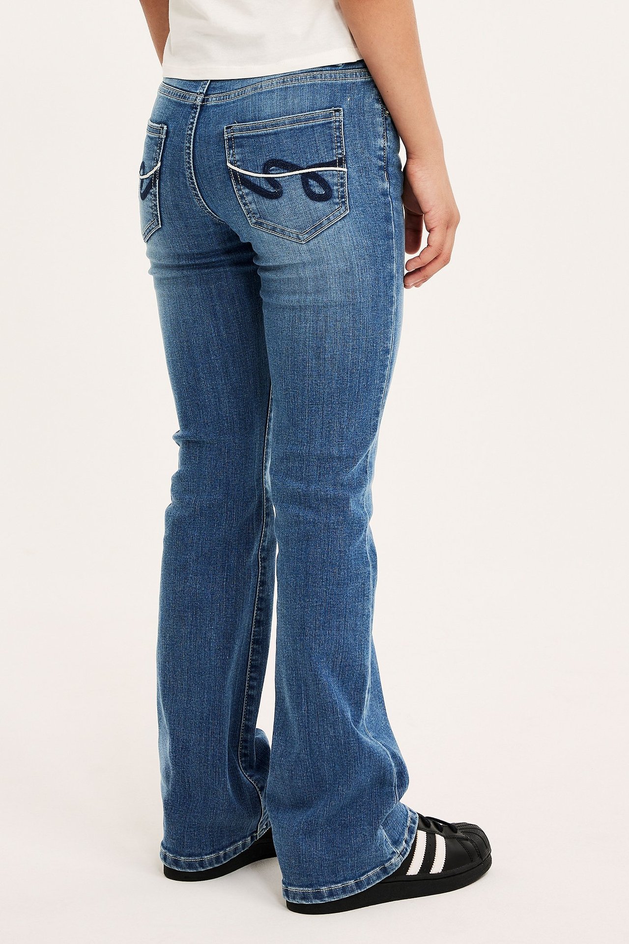 Dziecko w ciasnych jeansach bootcut z niebieskiego stretch denimu z haftem, niska talia.