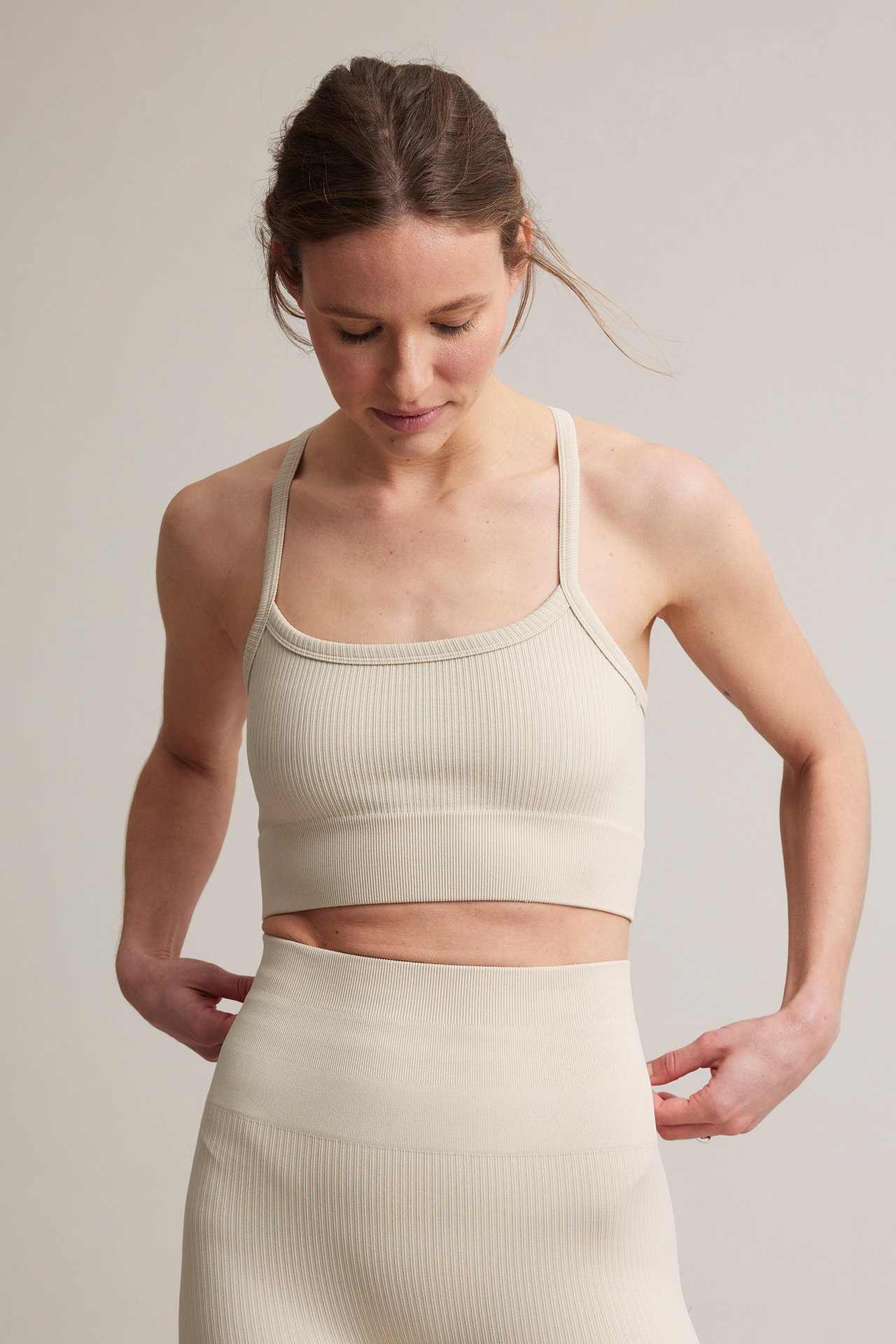 Frontbilde av en kvinne i en lys beige ribbet sømløs sports-BH og matchende høytlivs leggings.