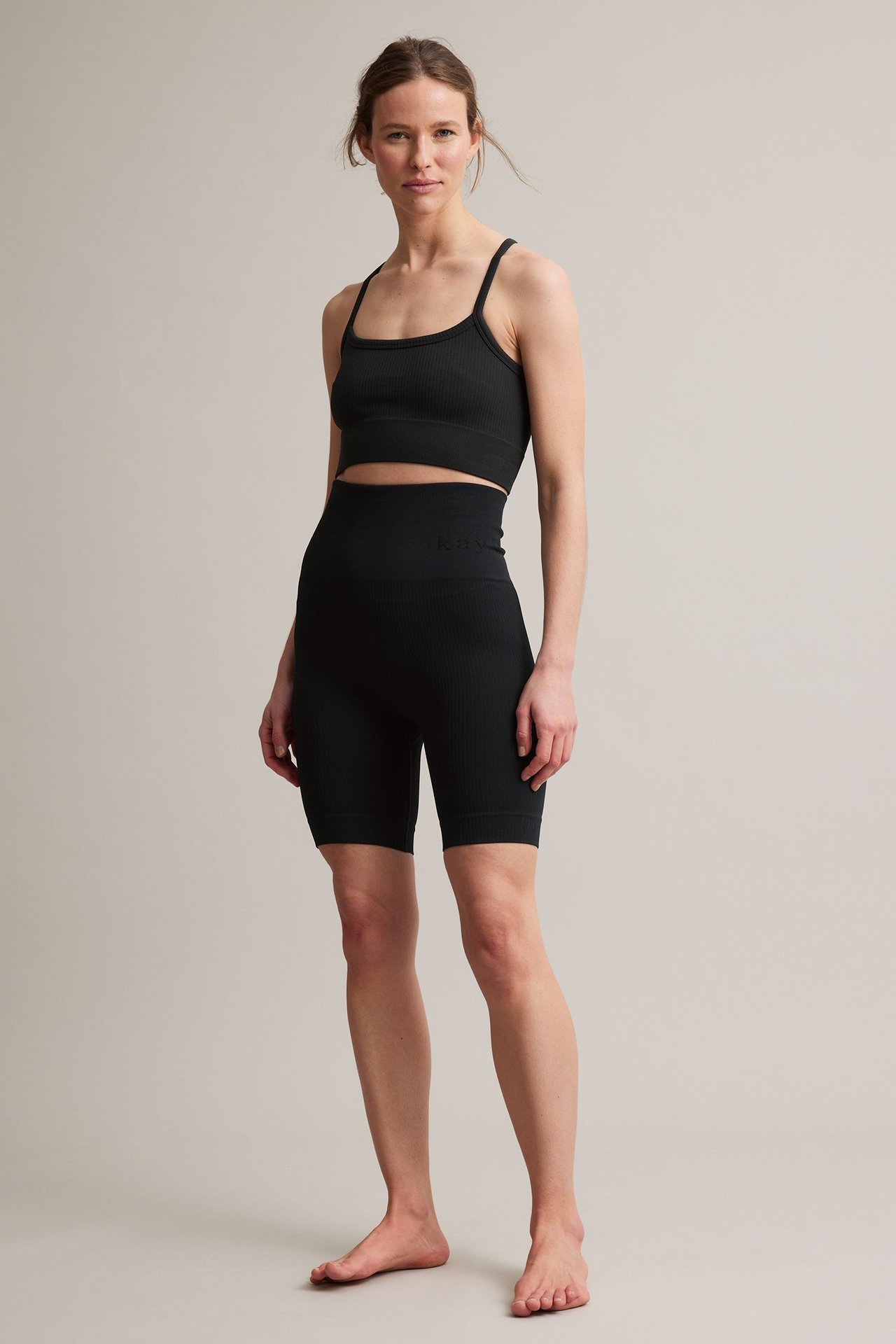 Forfra: kvinne i svart ribbet sømløs sports-bh og matchende høytlivs sykkelshorts.