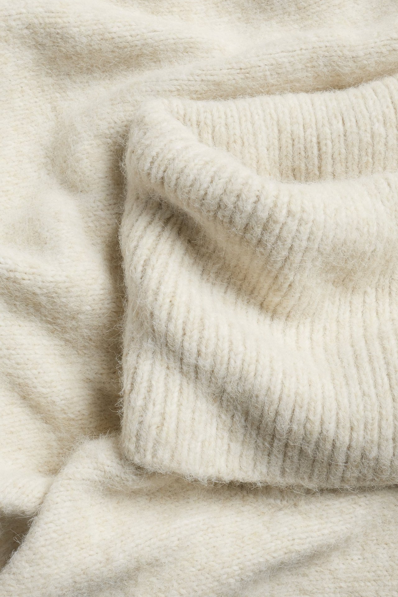 Zbliżenie beżowego melanżowego dzianinowego poncza z prążkowanym golfem.