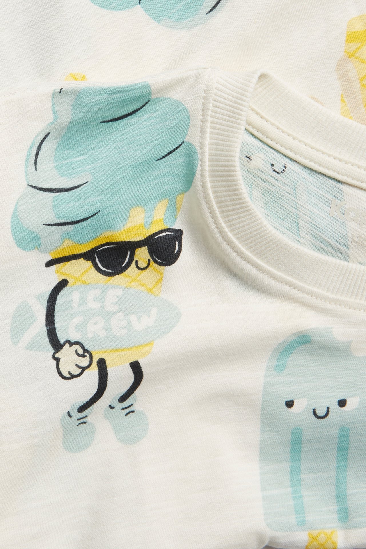 Zbliżenie na dziecięcy T-shirt z bawełny w kolorze złamanej bieli z nadrukiem lodów i prążkowanym dekoltem.