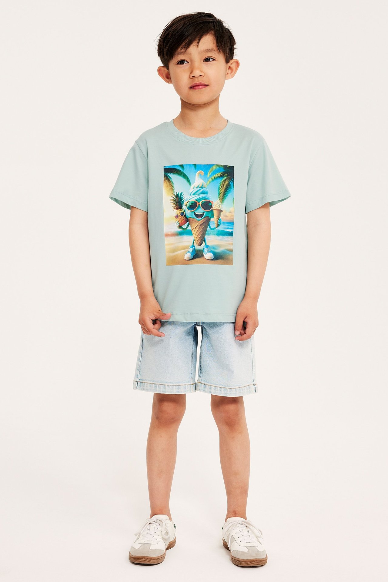 Framifrån: Barn i ljus turkos bomulls-T-shirt med glasstryck, ljusblå denimshorts och vita sneakers.