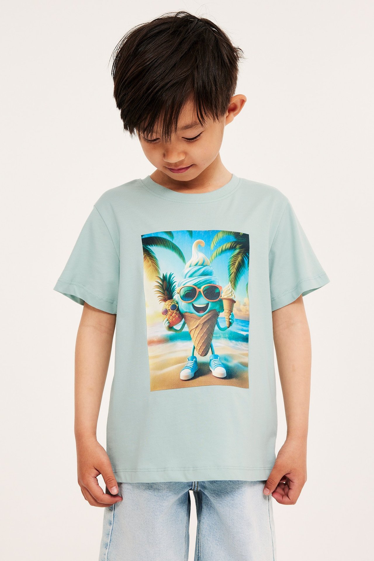 Framifrån, ett barn i ljus turkos bomulls-t-shirt med glasstryck och ljusblå denimshorts.