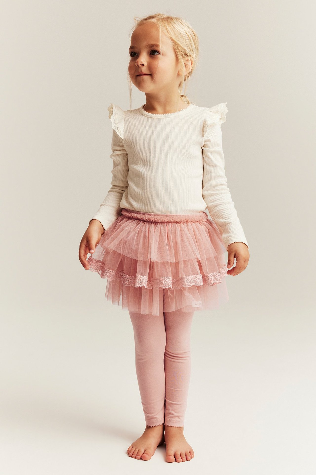 Frontvy av ett barn i rosa leggings med trelagers tyllkjol och en krämfärgad ribbad långärmad topp.