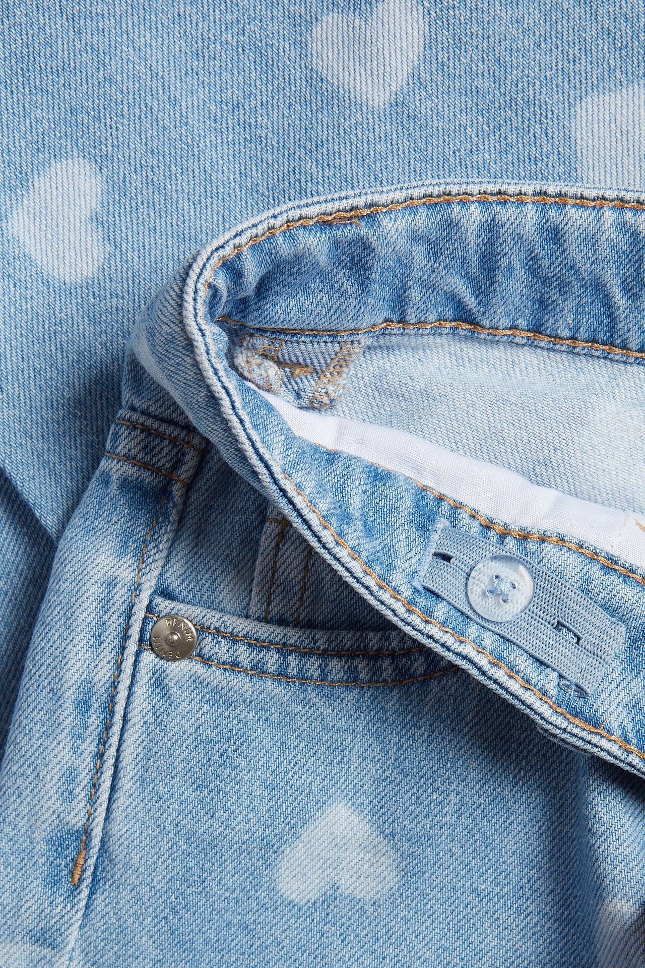 Zbliżenie na jasnoniebieskie szerokie jeansy z denimu z białymi sercami i regulowanym guzikiem w pasie.