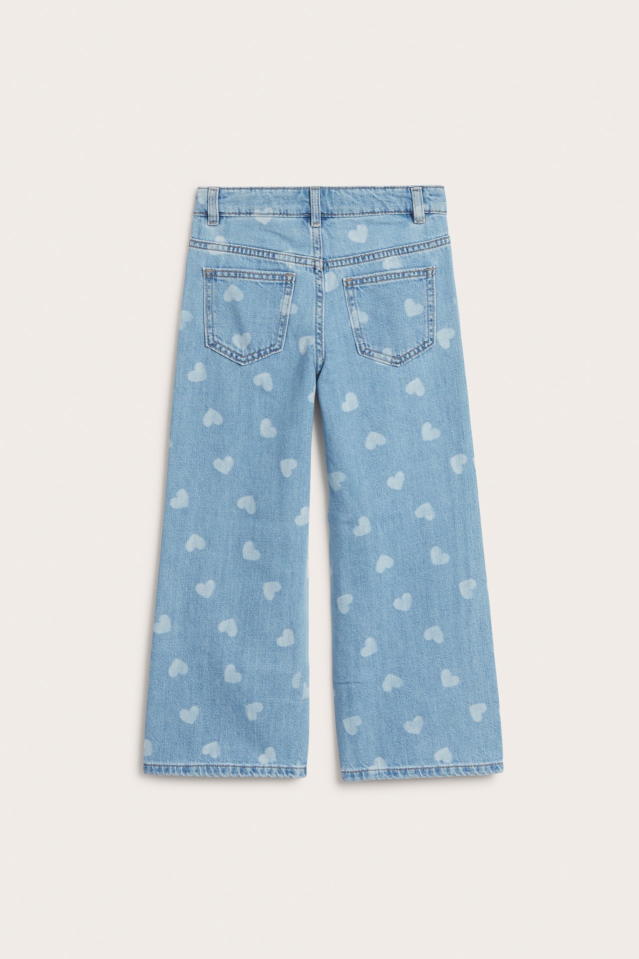 Bakifrån: vida jeans för barn i ljus denim med vita tryckta hjärtan och två bakfickor.