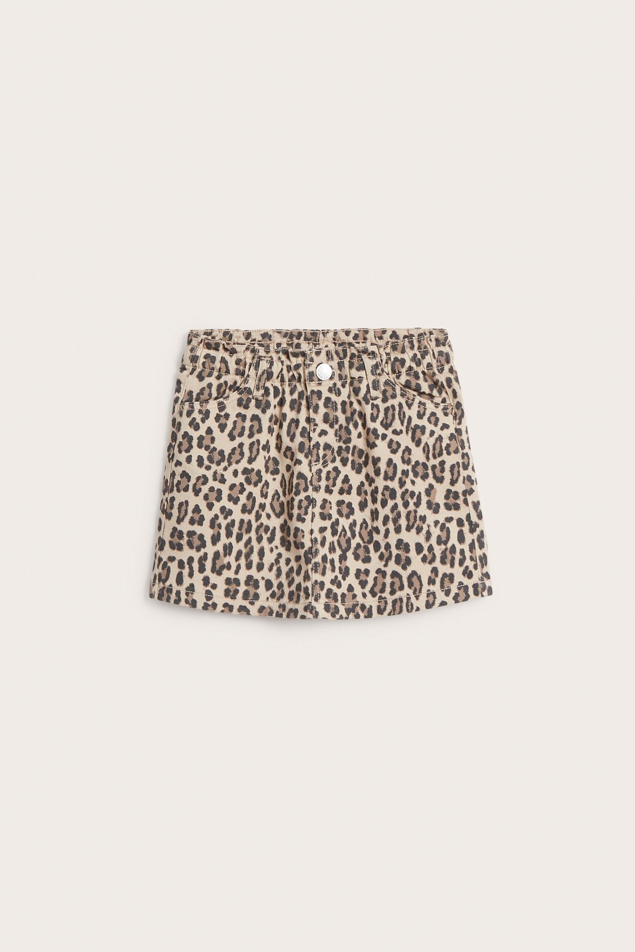 Framifrån: kort beige bomullstwillkjol för barn med leopardmönster, resår i midjan och knapp.