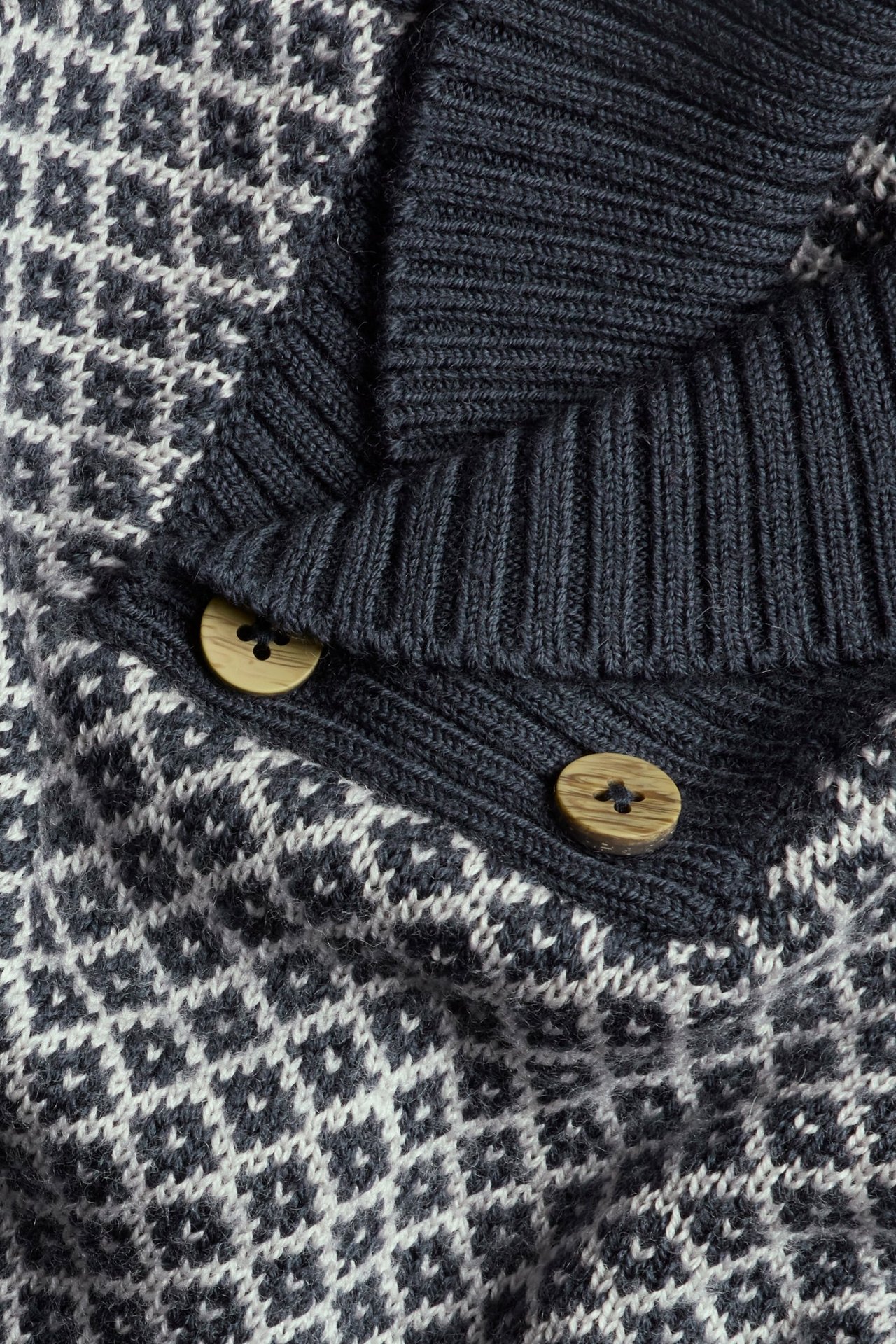 Zbliżenie na granatowy i biały wzorzysty sweter wełniany z kołnierzem szalowym i dwoma drewnianymi guzikami.
