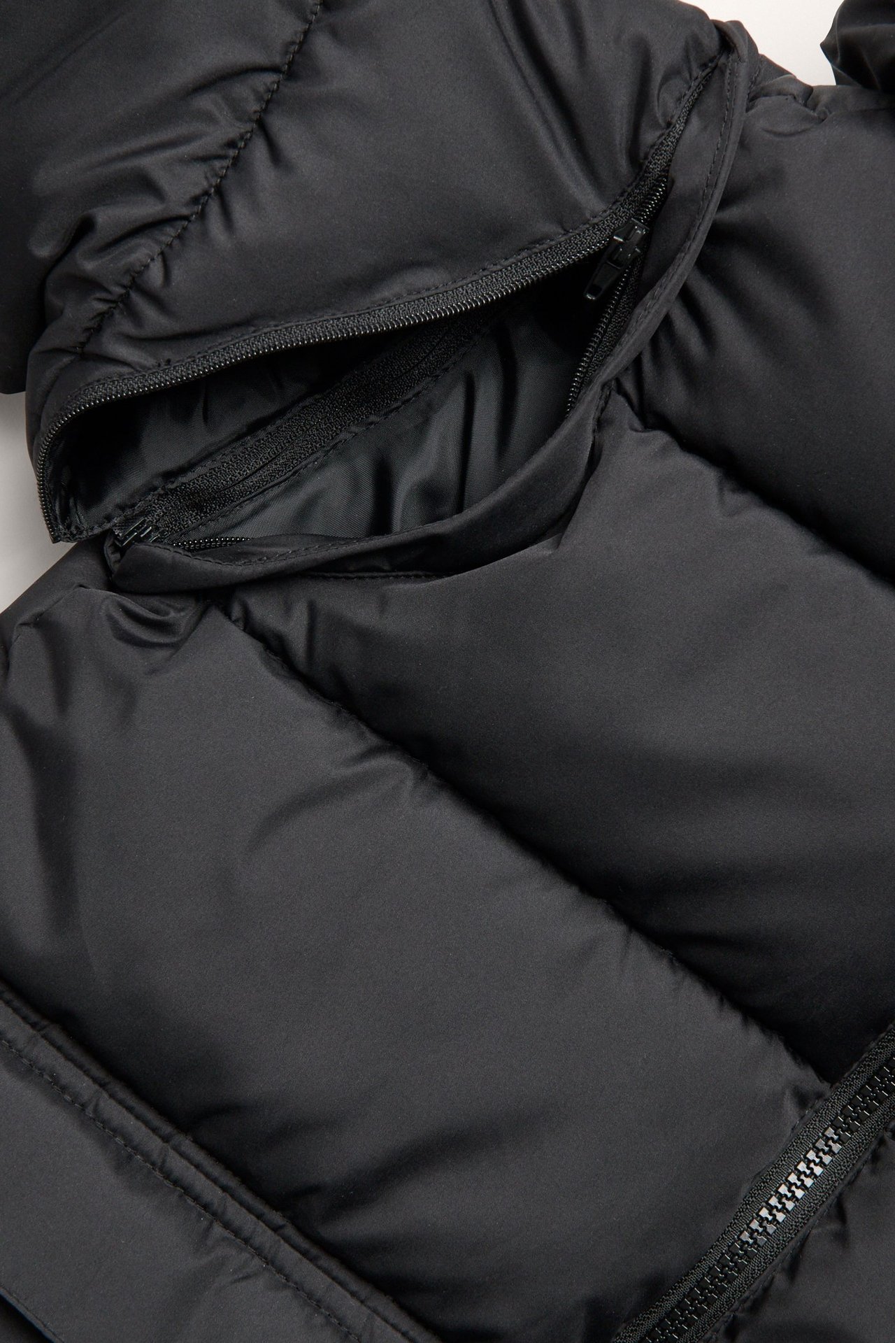Zbliżenie czarnej pikowanej kurtki puchowej z widocznym zamkiem błyskawicznym na odpinany kaptur.