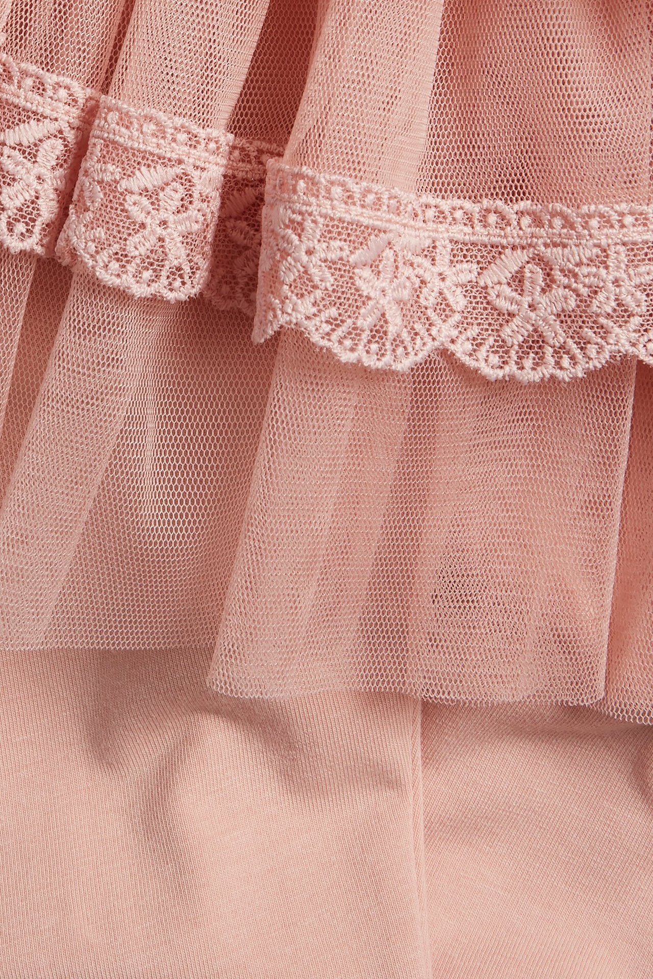 Lähikuva vaaleanpunaisista puuvillaleggingsista, joissa on kiinnitetty röyhelötyllihame ja pitsireunus.
