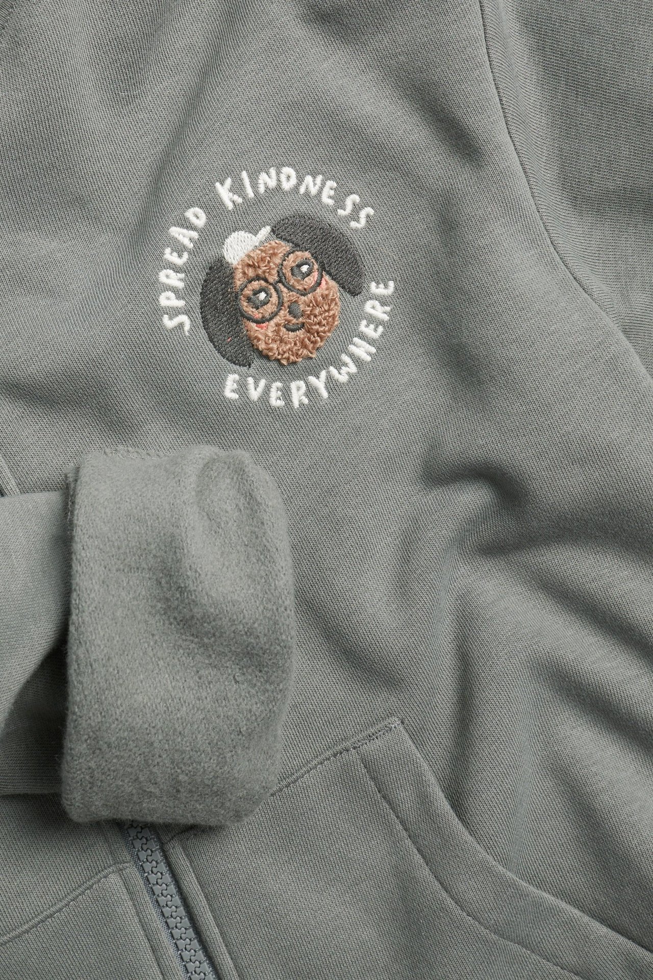 Zbliżenie na szarą bluzę dziecięcą z zamkiem, kieszeniami i haftem psa "Spread Kindness Everywhere".