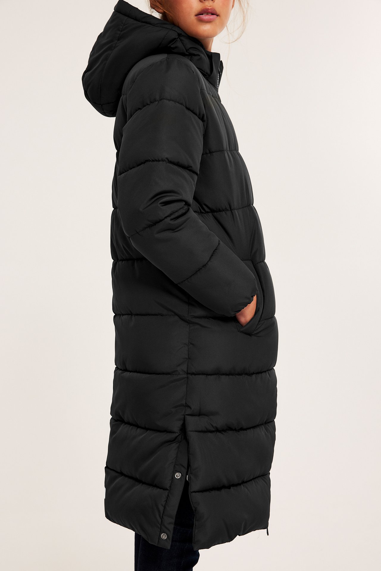 Sidebilde av et barn i lang svart boblejakke med hette og mørke jeans, hender i lommer.